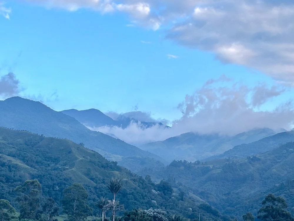 A landscape of green mountains with clouds and a blue sky.