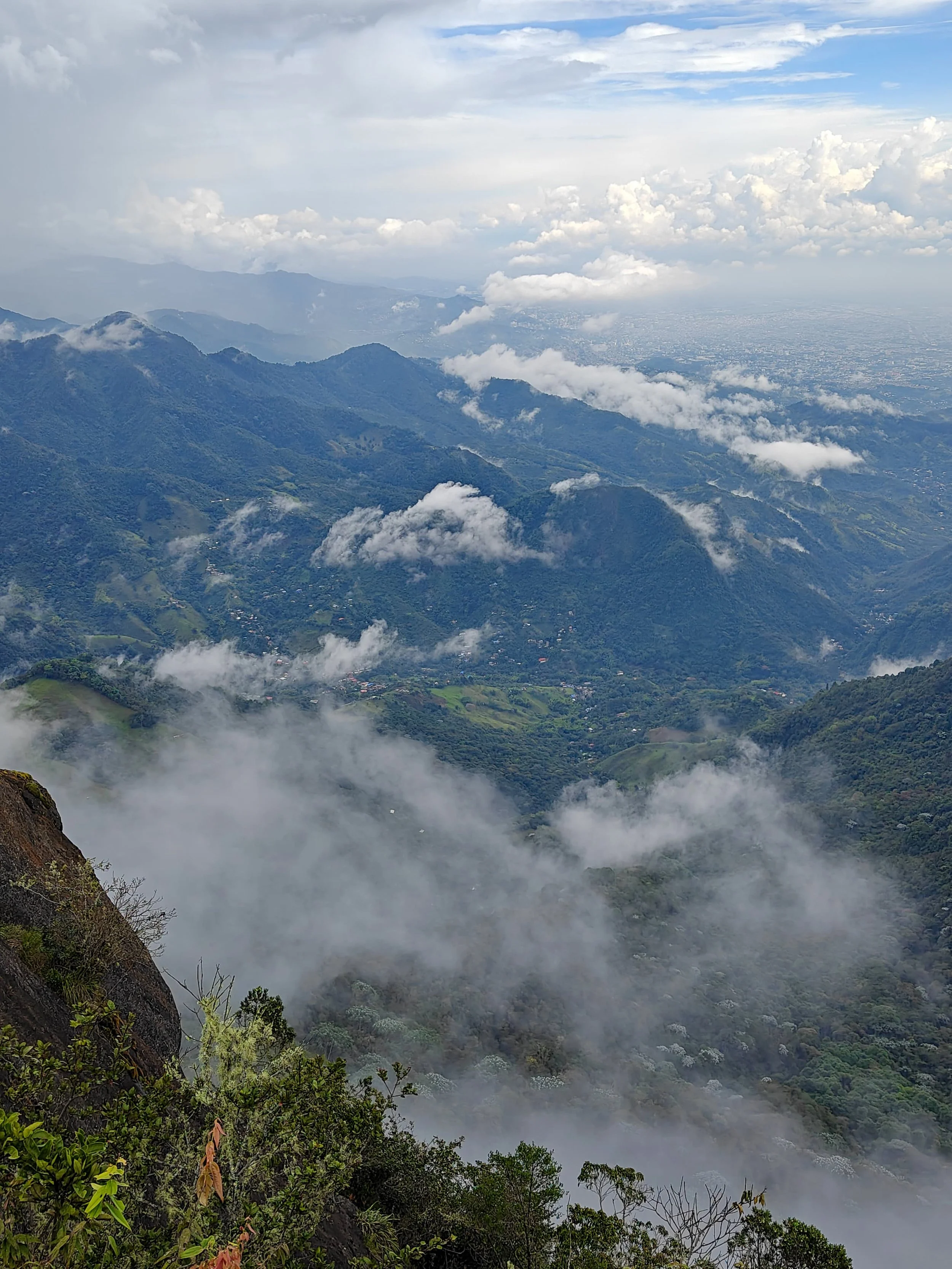 A scenic view of green mountains shrouded in clouds and mist, with a cloudy sky overhead.