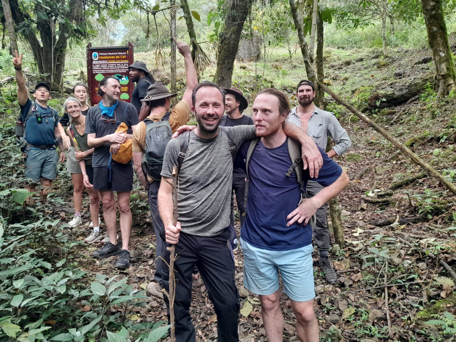 A group of people hiking in a forest, with some smiling and posing for the photo, surrounded by green trees and plants.