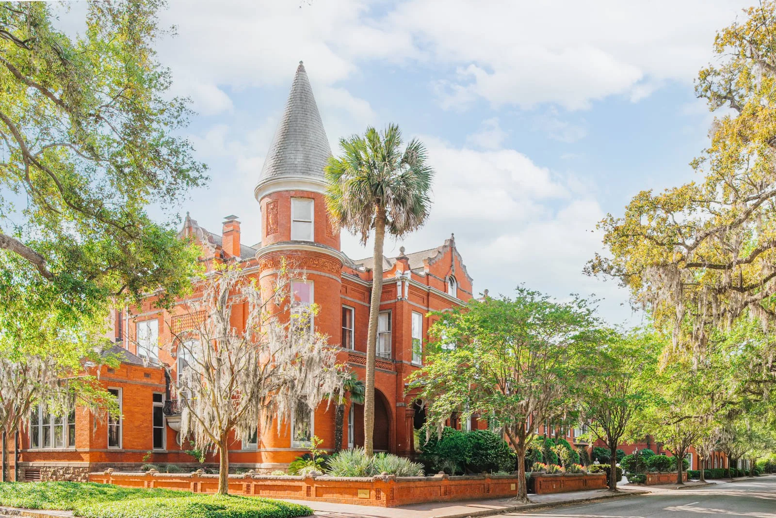 Historic red brick Victorian mansion exterior surrounded by palm trees and Spanish moss in Savannah.