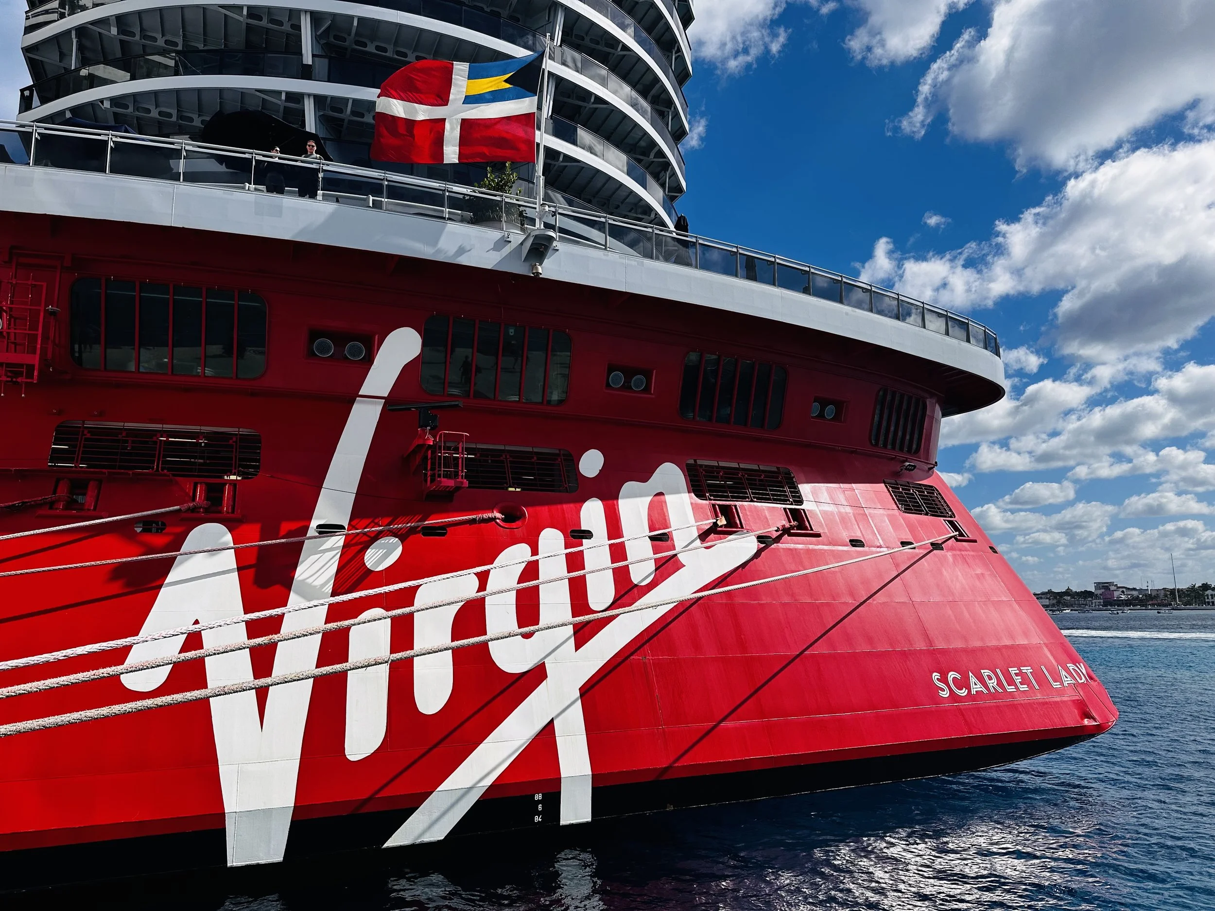 Exterior of the Scarlet Lady cruise ship docked in turquoise water.