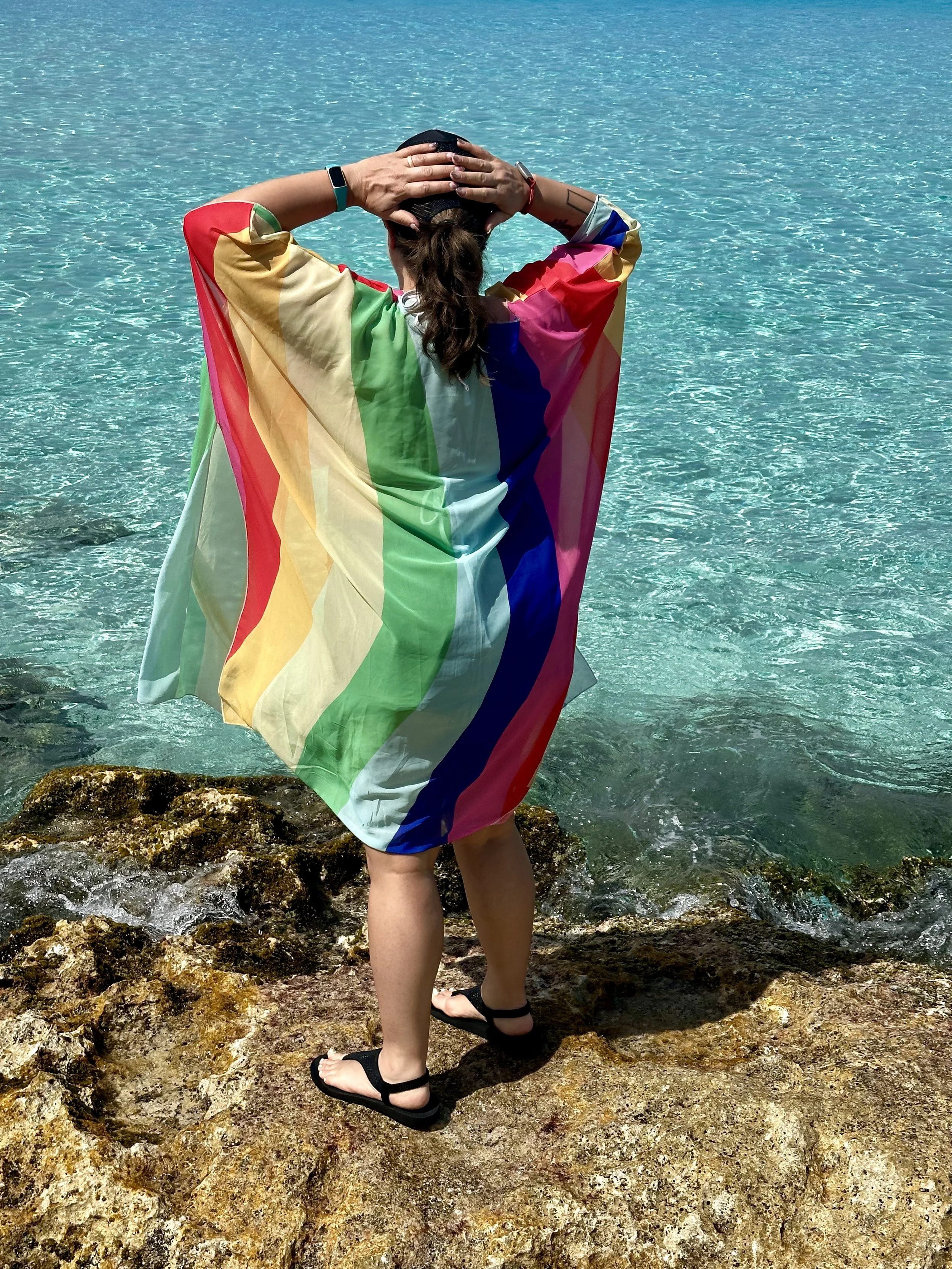 Woman wearing a rainbow cape looking at the ocean on a Virgin Voyages cruise, representing the inclusive and LGBTQ+ friendly atmosphere.
