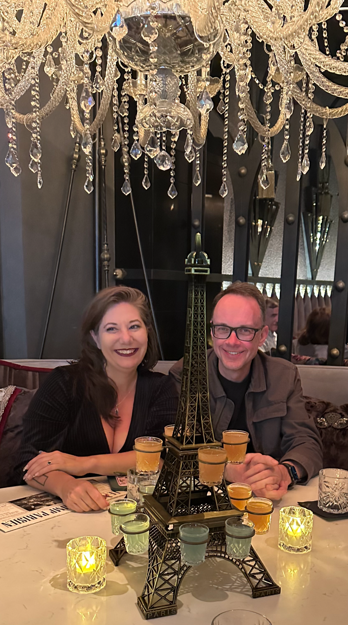 Follow the Goose Travel founder Caitlin and her husband Aaron smiling at a candlelit restaurant table under a crystal chandelier.