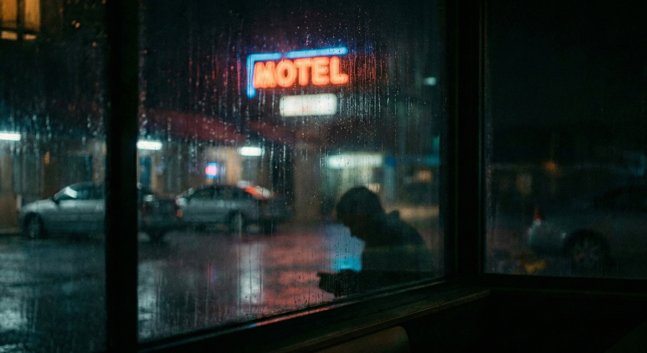 Rainy city street at night viewed through a hotel window, representing the risks of booking unvetted travel online.