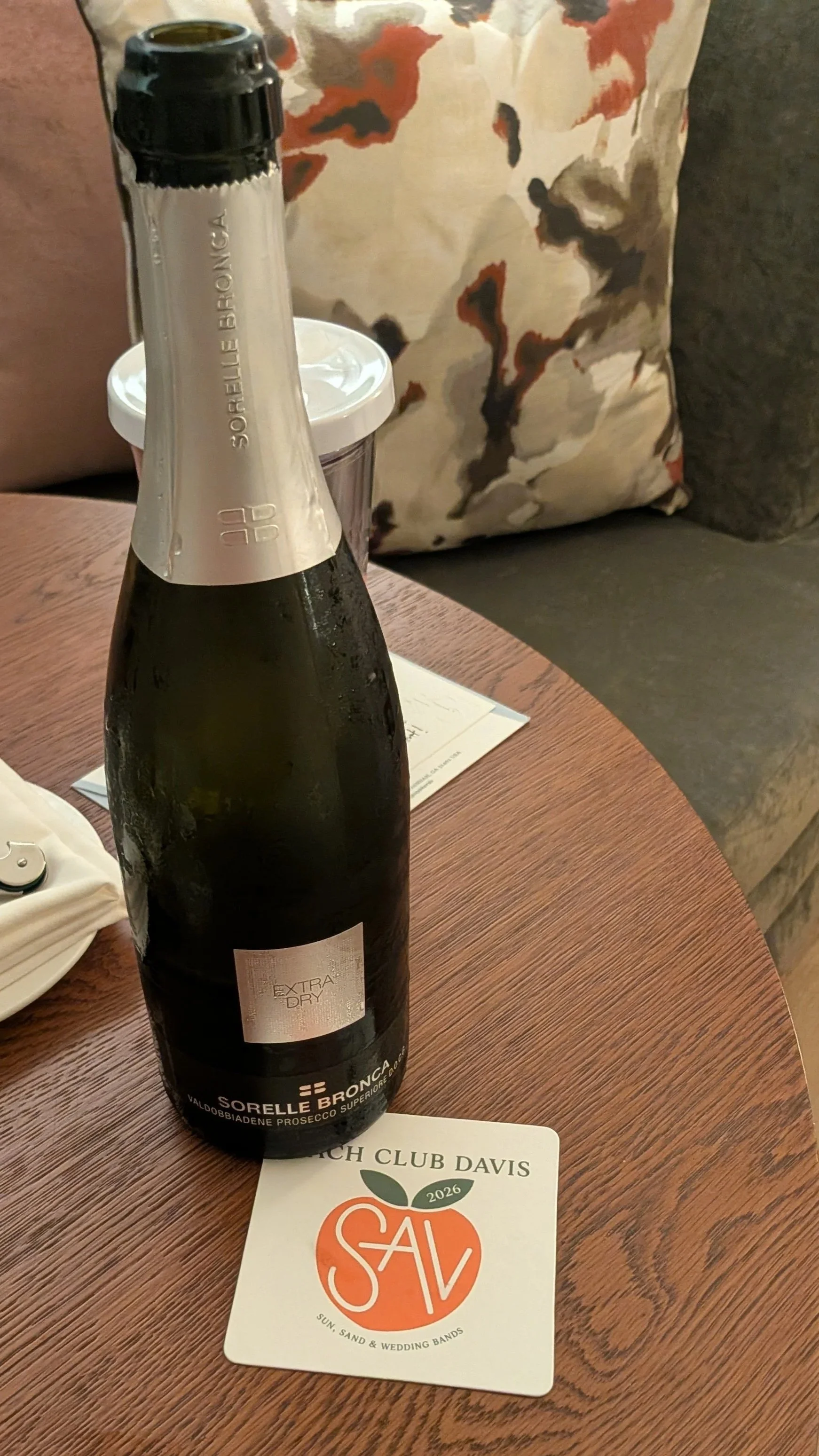 Chilled bottle of Sorelle Bronca Prosecco welcome gift on a wooden table with a custom Savannah bachelorette coaster.