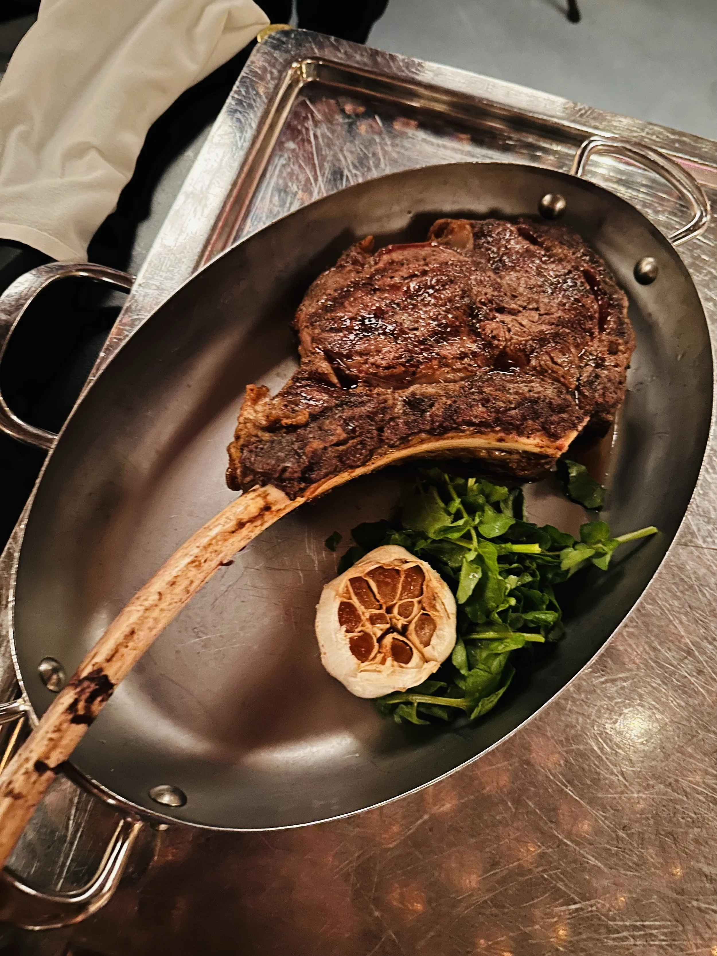 A massive Tomahawk steak served table-side at a Virgin Voyages restaurant, showing the high quality of food.