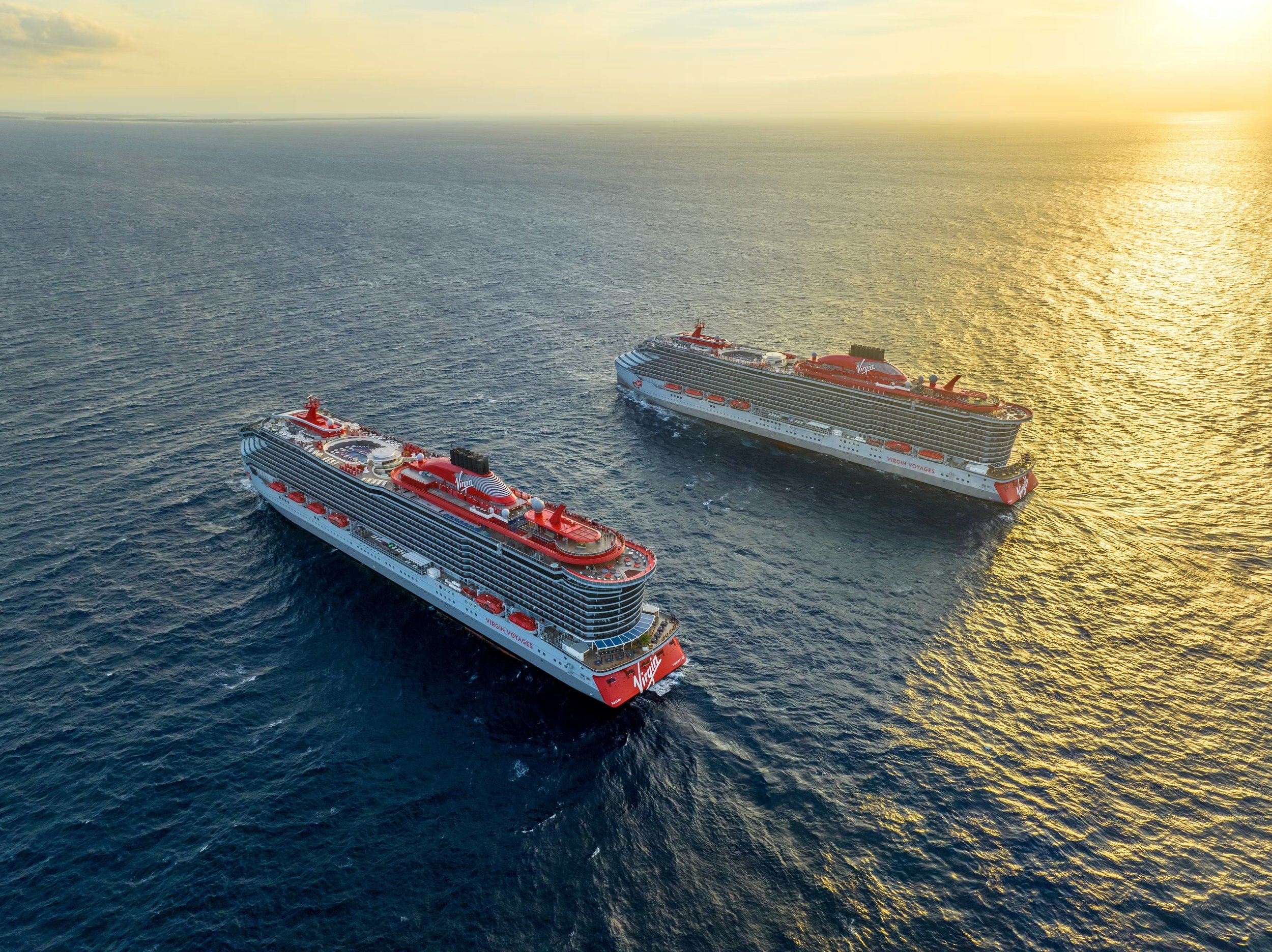Aerial view of two Virgin Voyages cruise ships sailing side by side at sunset for a fleet meetup.