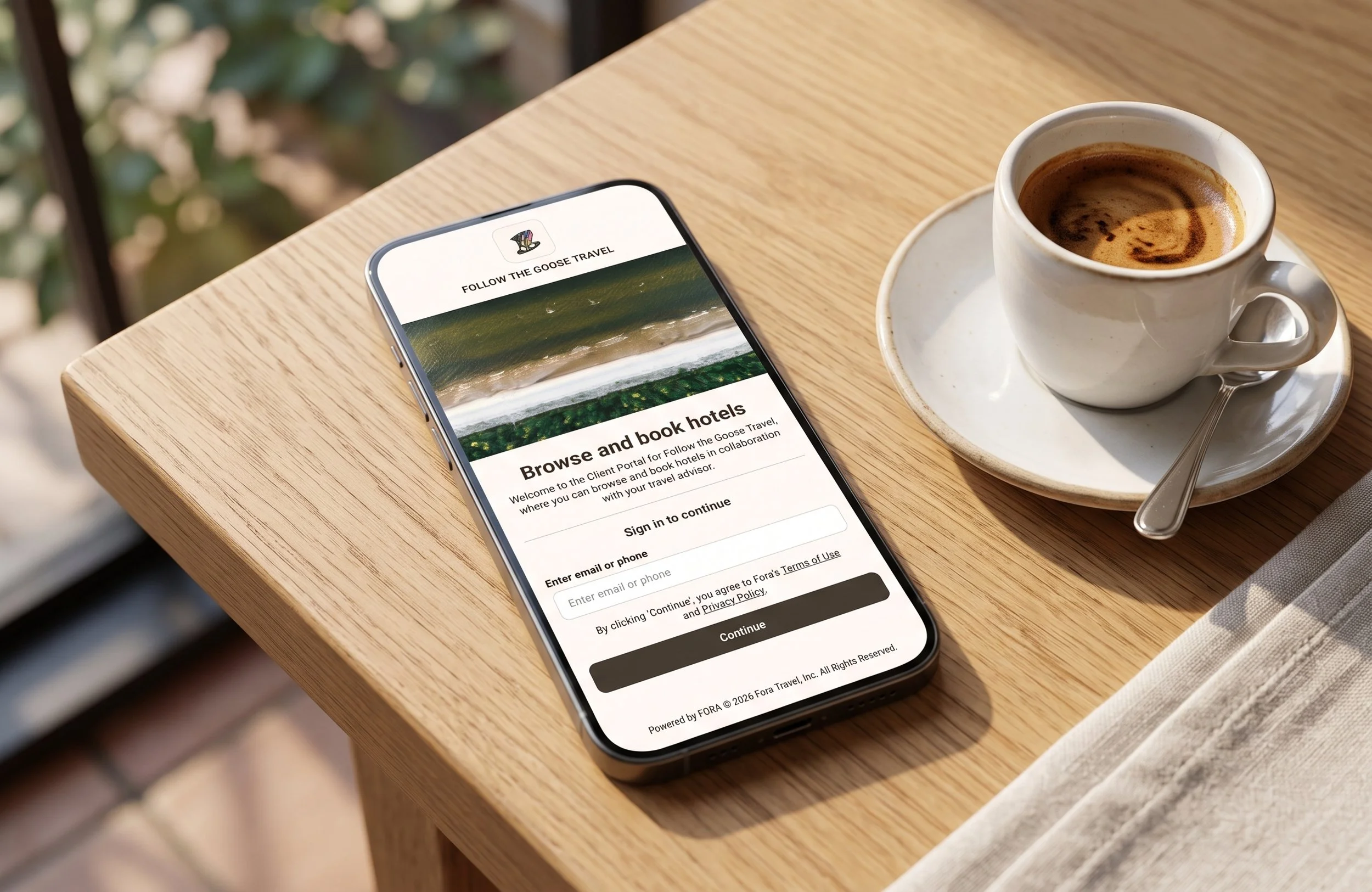 A close-up of a smartphone displaying the FTG Travel Client Booking Portal interface, sitting on a sunlit wooden cafe table next to a fresh cup of espresso.
