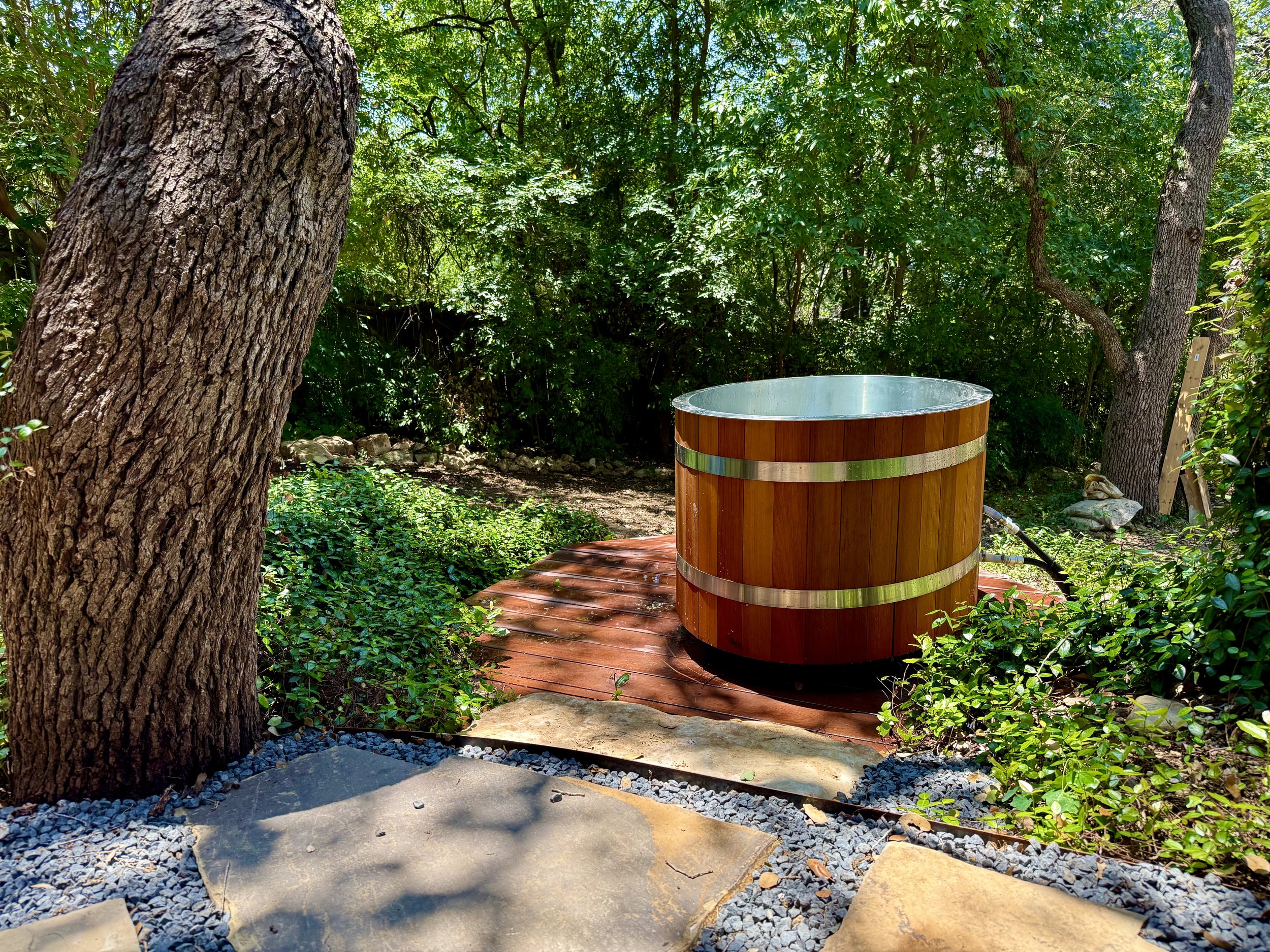 A wooden hot tub on a deck in a lush, green forested area.