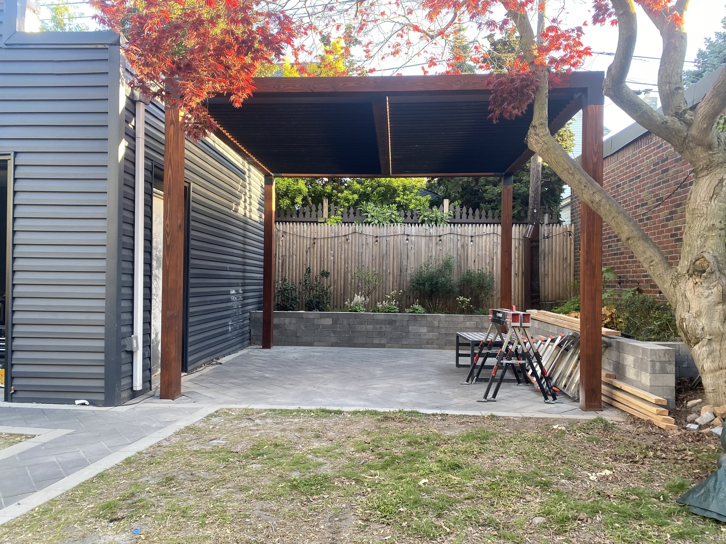 A sleek, modern pergola with an articulating louvered roof, allowing for customizable shade and airflow. Built with stained hardwood posts, black anodized aluminum louvers and steel corner brackets.