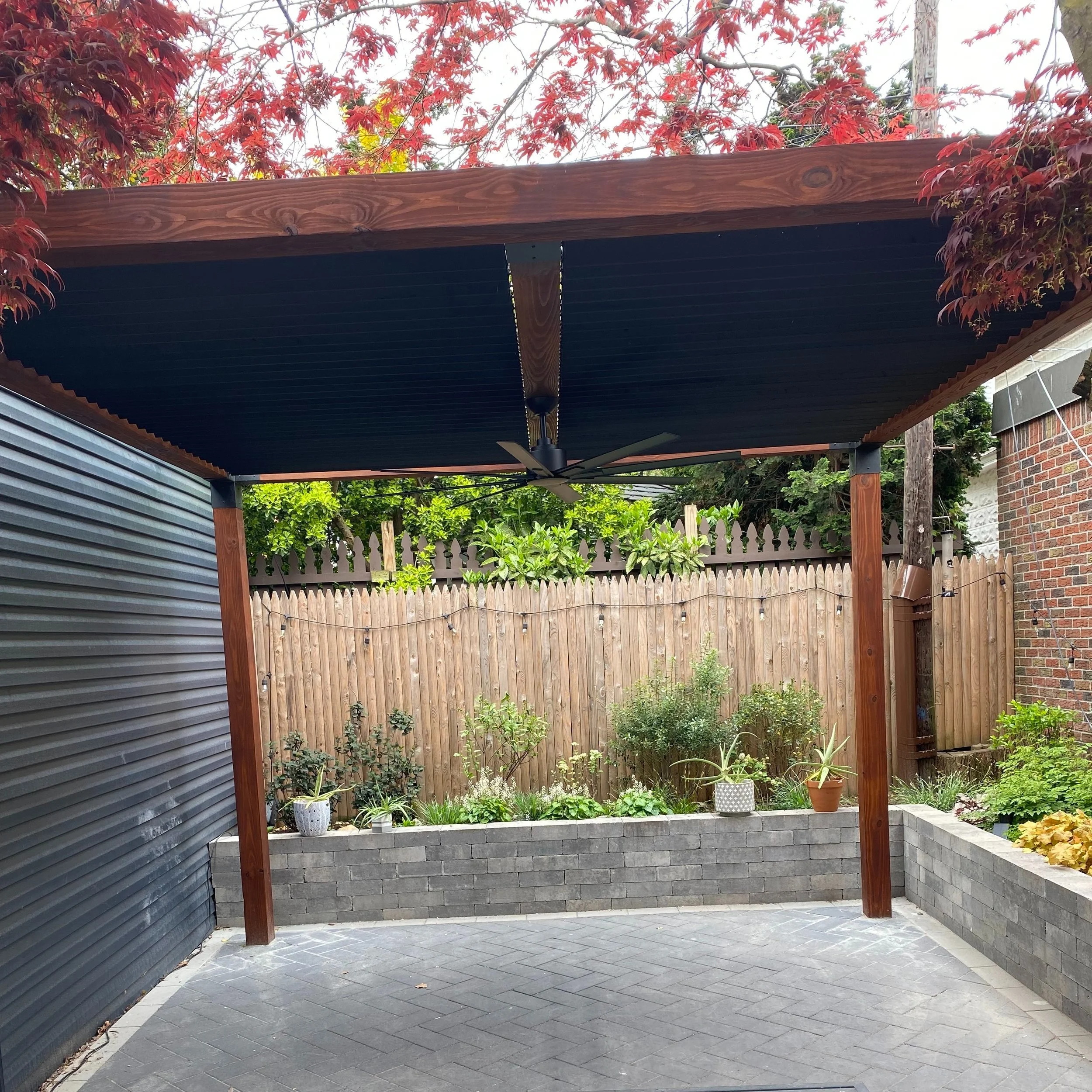 A sleek, modern pergola with an articulating louvered roof, allowing for customizable shade and airflow. Built with stained hardwood posts, black anodized aluminum louvers and steel corner brackets.