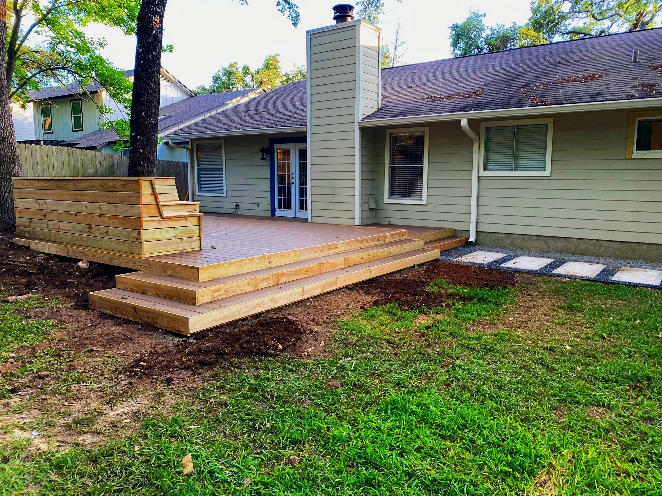 Composite ground level deck with a built-in cedar bench dining area and wrap-around stairs. A raised gravel pavilion was built beside the deck to accommodate a fire-pit and grill. A walkway leading off the property features custom concrete pavers.