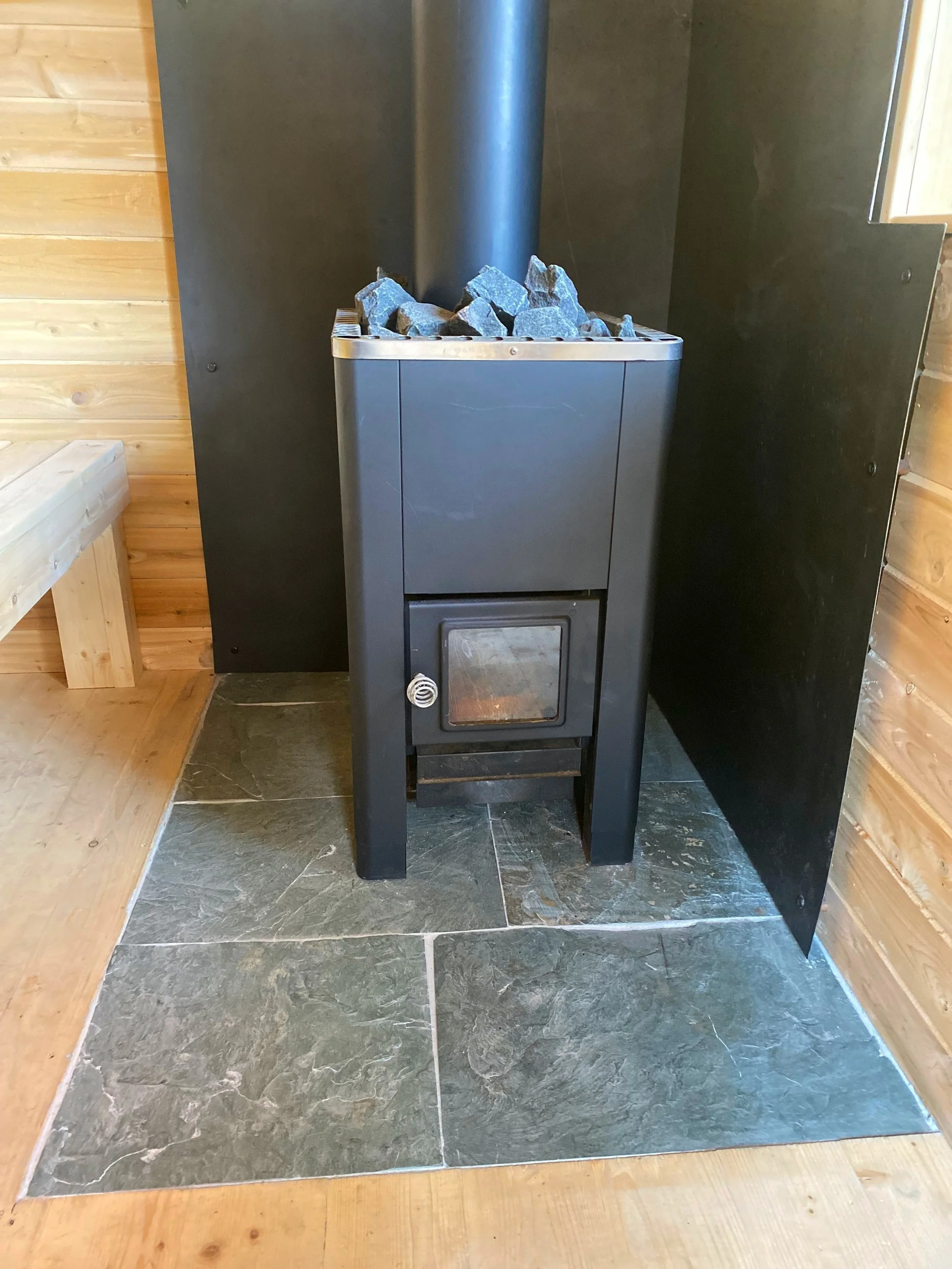 A large window frames sweeping valley views in this handcrafted sauna, featuring a native stone hearth and cedar interior.