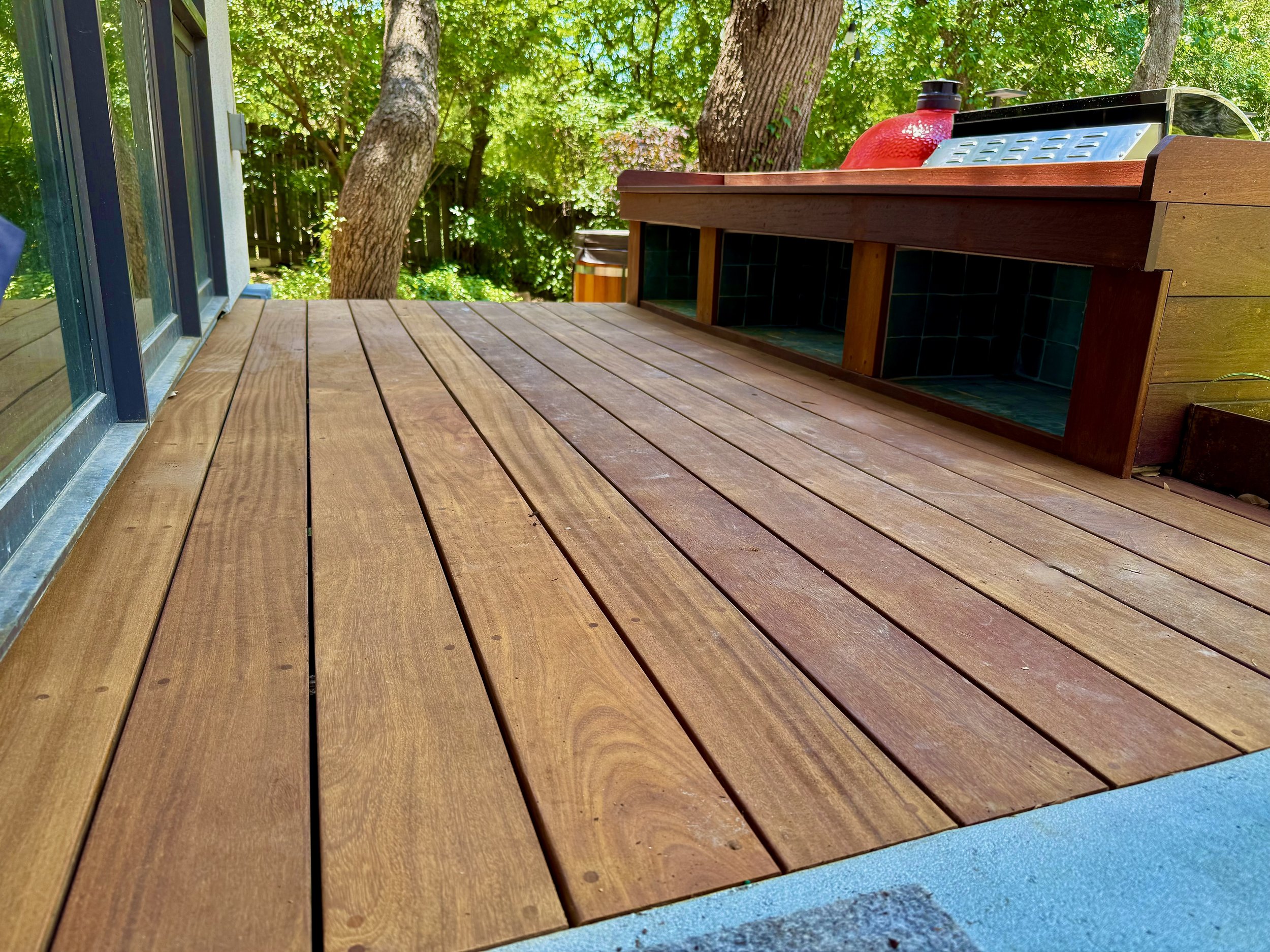 A wooden deck with a built-in barbecue area and a view of trees and greenery in the background.