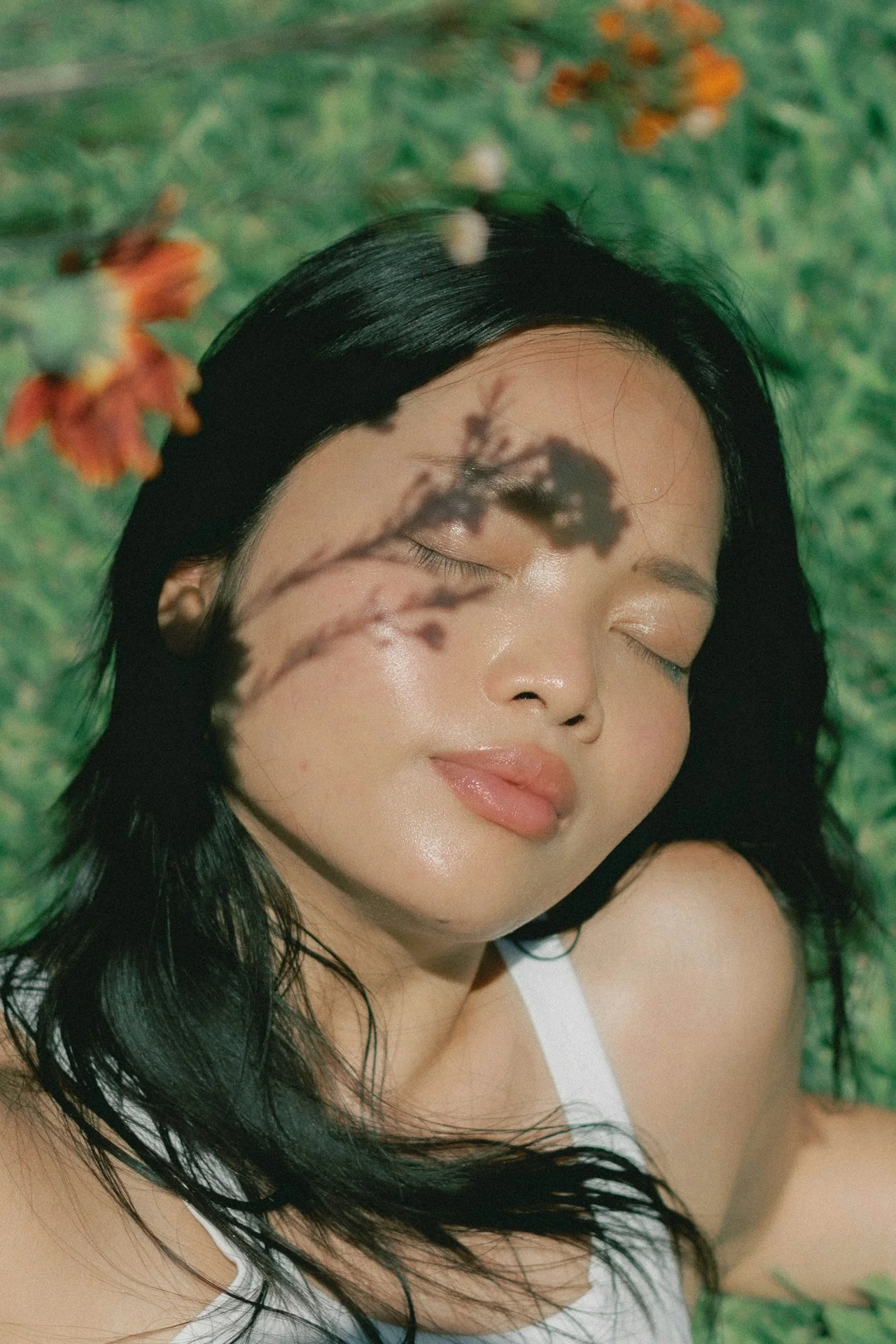Woman with eyes closed and face lifted toward sunlight, with soft floral shadows across her skin, representing calm and nervous system regulation in trauma-informed therapy.