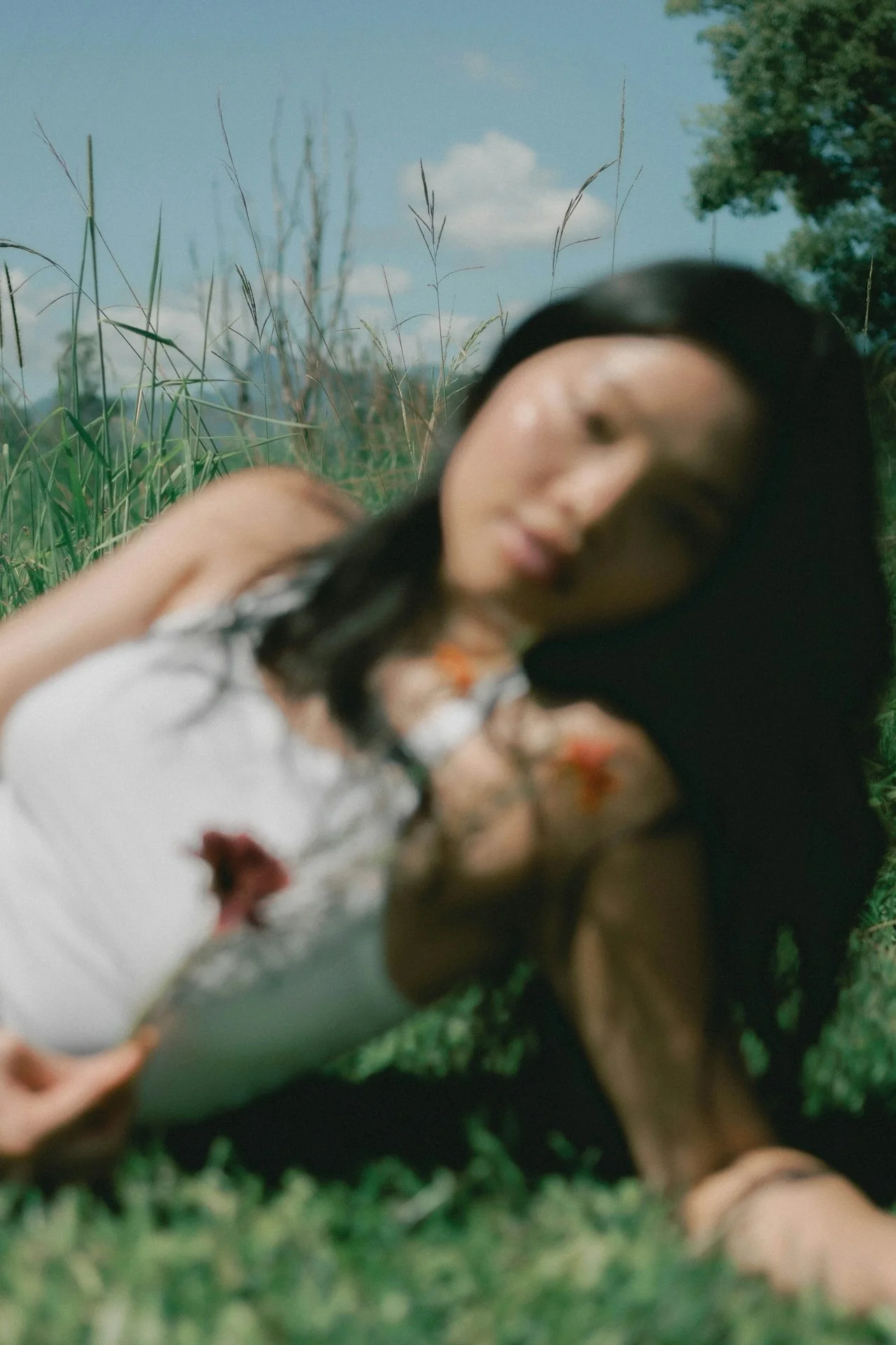 Woman lying in sunlit grass holding a flower, representing calm and emotional healing through EMDR therapy.