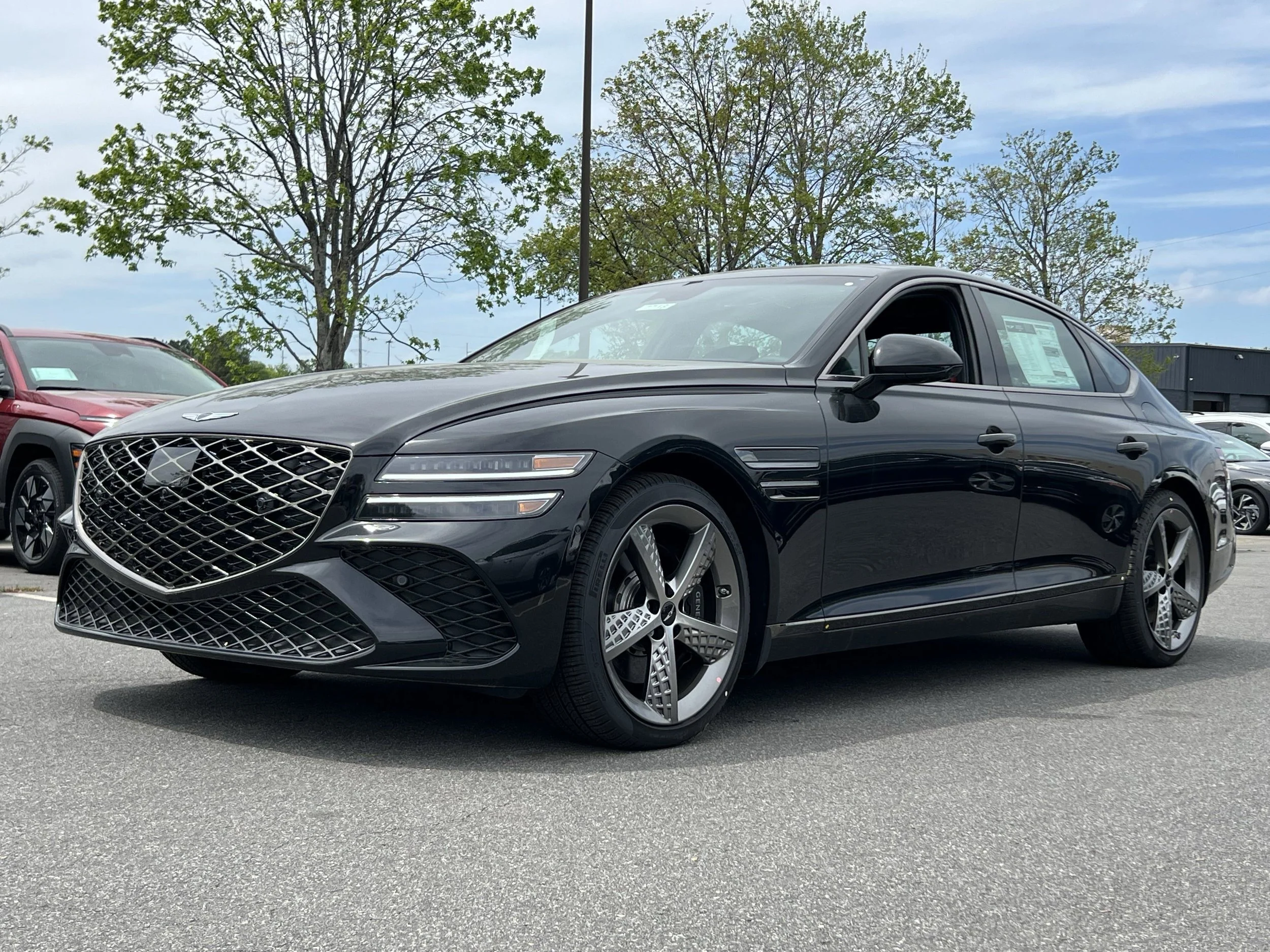 Black luxury sedan parked in a lot with trees and other vehicles in the background.