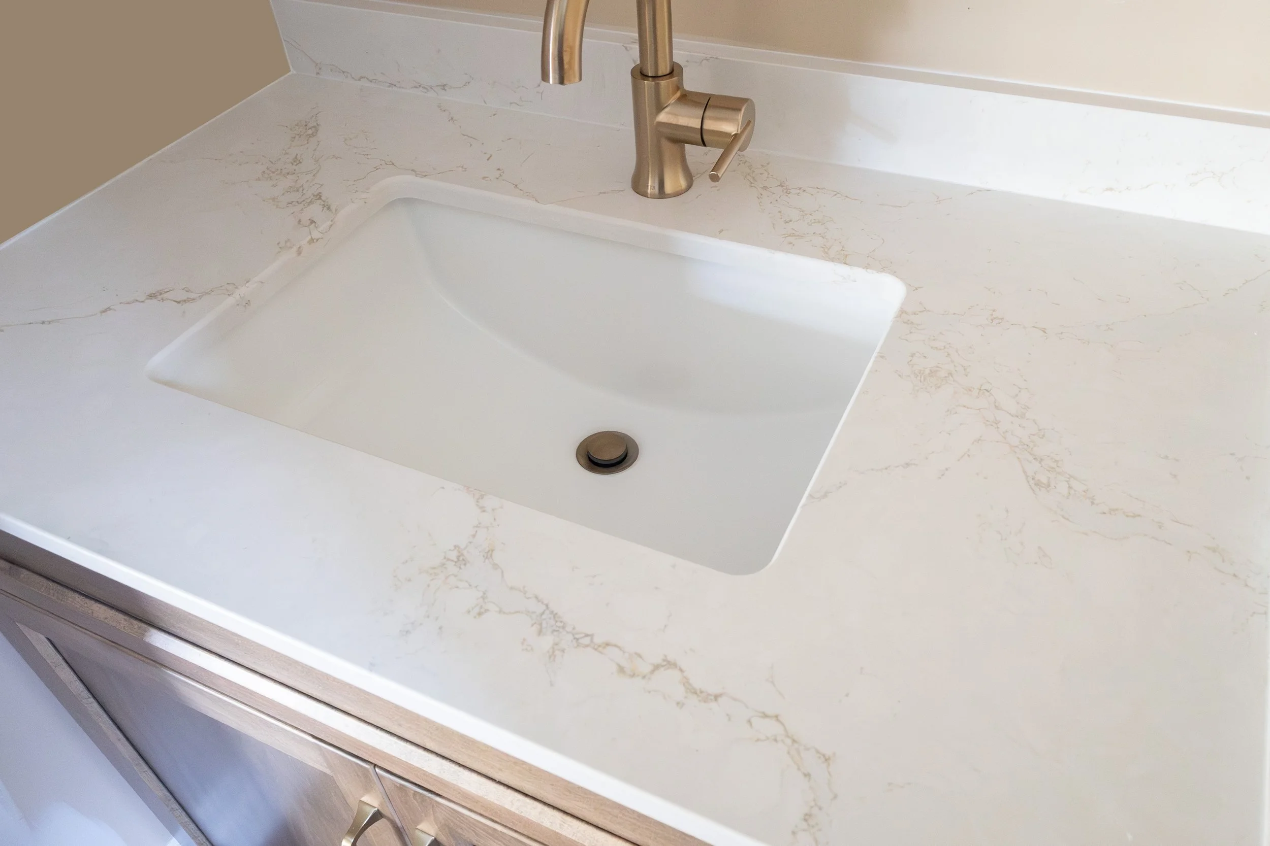 White kitchen sink with a modern brushed nickel faucet installed in a beige and white marble countertop with a backsplash.