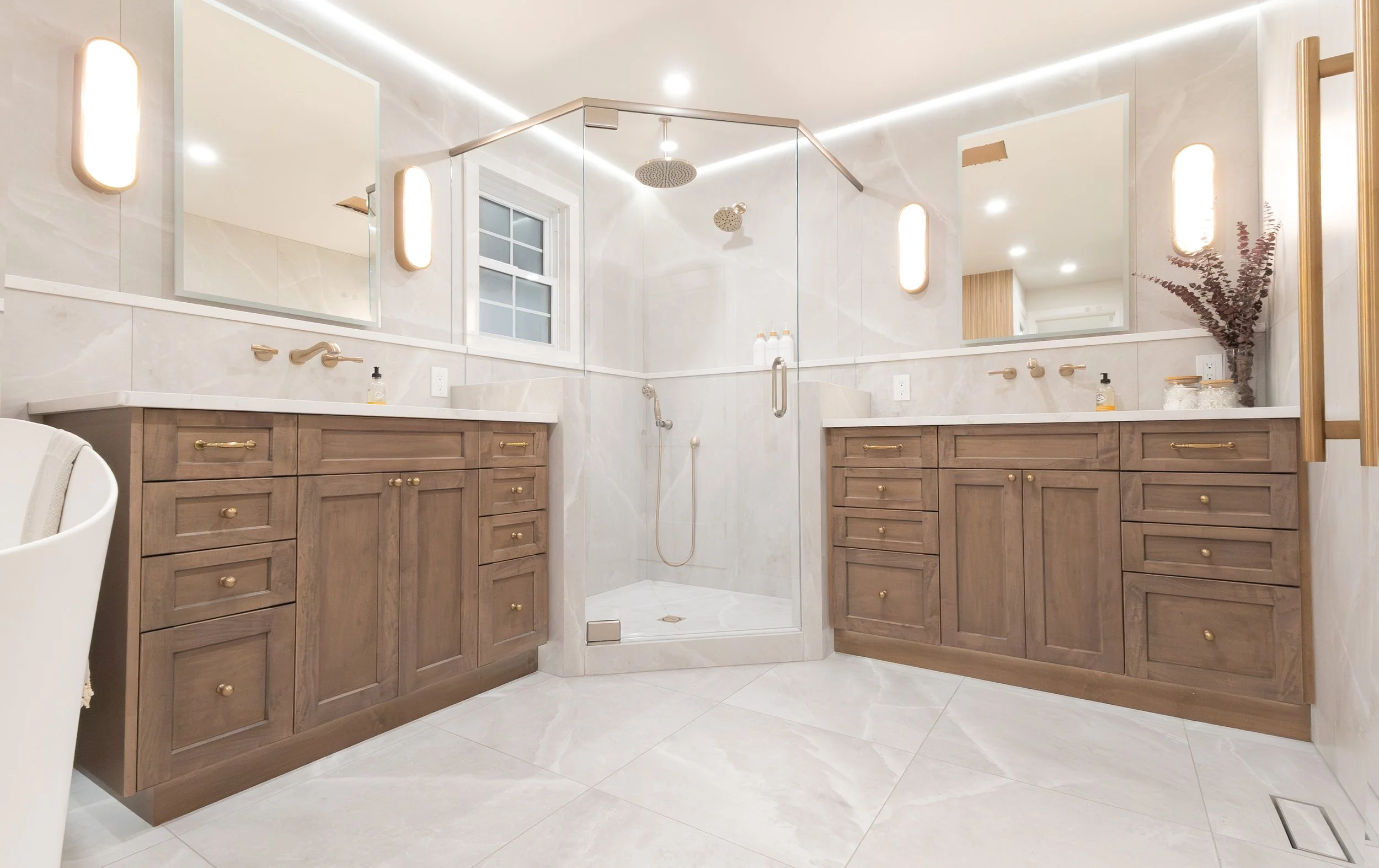 Modern bathroom with double vanity, large mirror, and walk-in shower with glass enclosure, beige marble tiles, and minimalist decor.