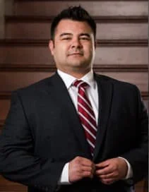 A man in a suit and tie standing in front of a wooden background.