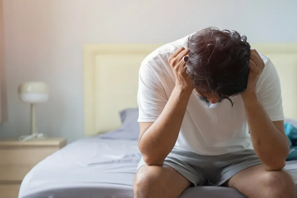 A man in distress while sitting by the edge of his bed