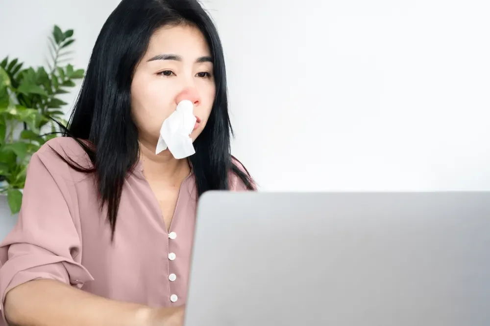 A woman with allergic rhinitis while working on her laptop