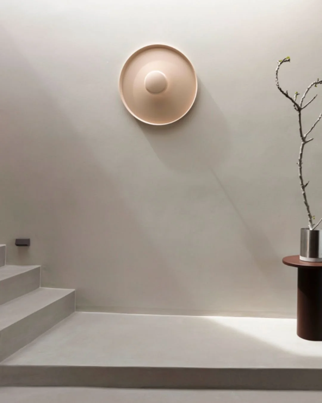 Minimalist interior with a staircase, a circular wall decor, a branch in a metallic vase, and soft lighting