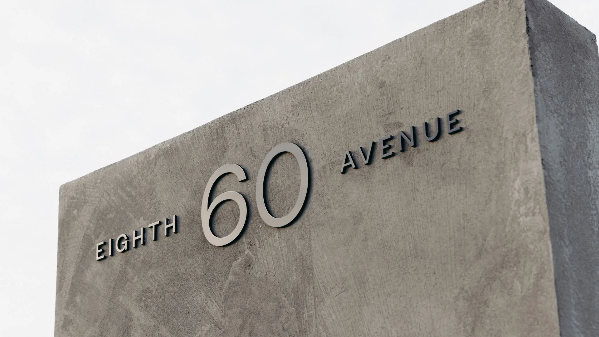 Close-up of a beige concrete structure displaying the street address 'EIGHTY 60 AVENUE' in black three-dimensional letters.