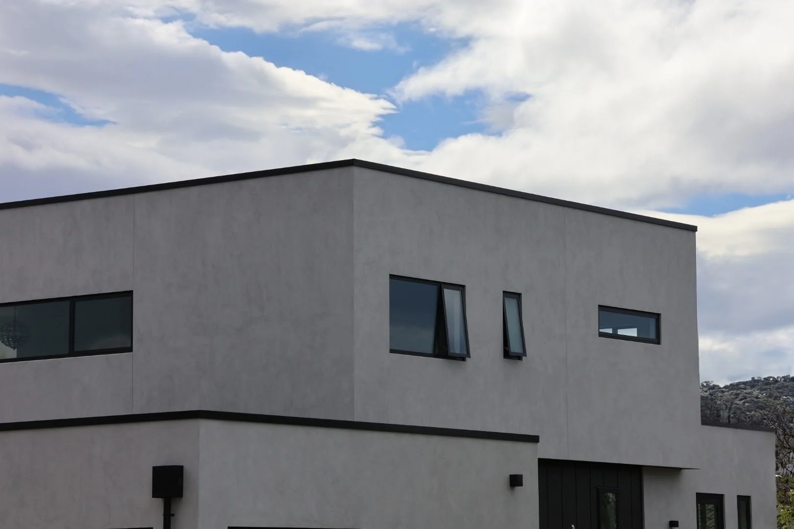 Modern white building with black trim and variously sized windows under a partly cloudy sky.