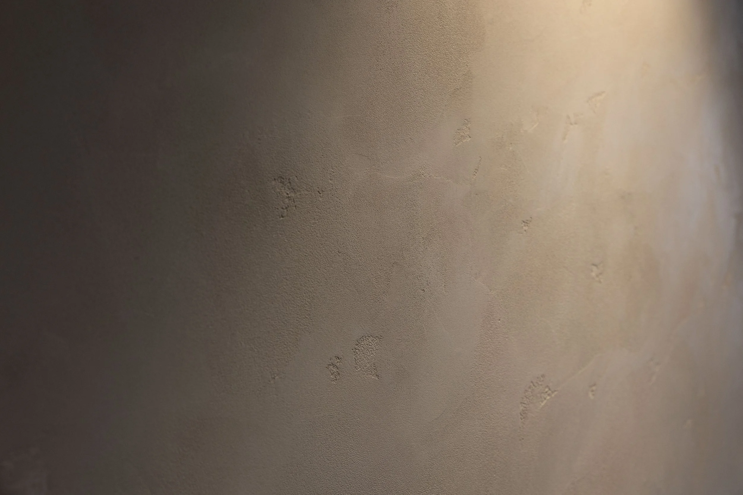 Close-up of a beige, textured wall with small imperfections and uneven patches.