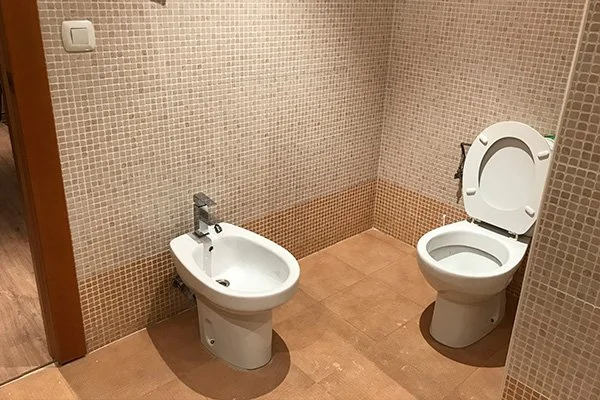 Bathroom with a bidet and toilet, both with white seats, in a room with tiled walls and floor.