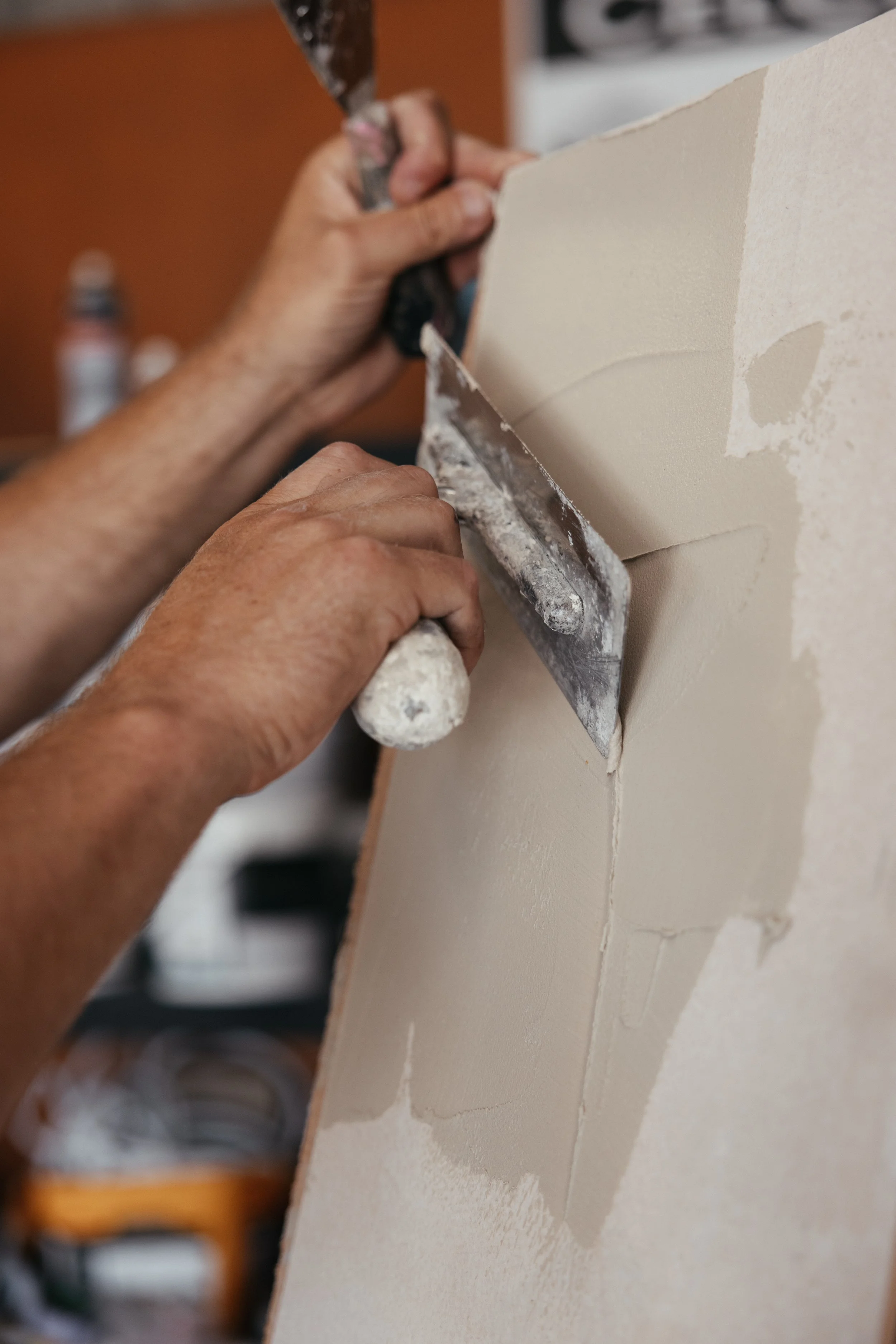 A person applying joint compound to drywall with a putty knife.