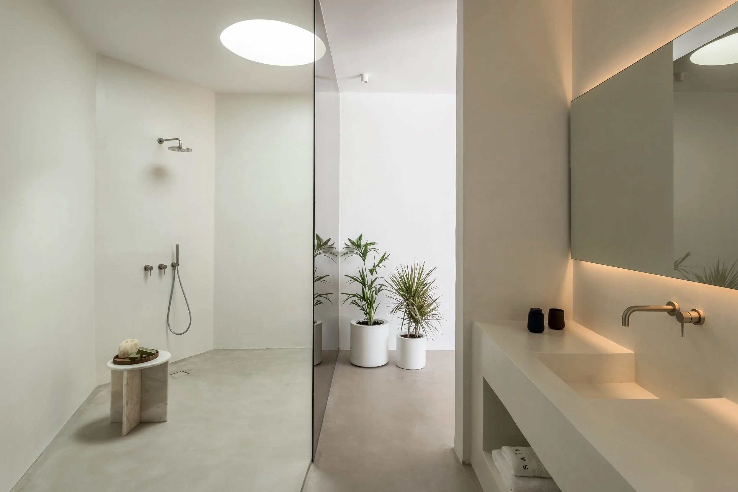 Microcement bathroom with walk-in shower, large mirror, white sink, and potted plants.