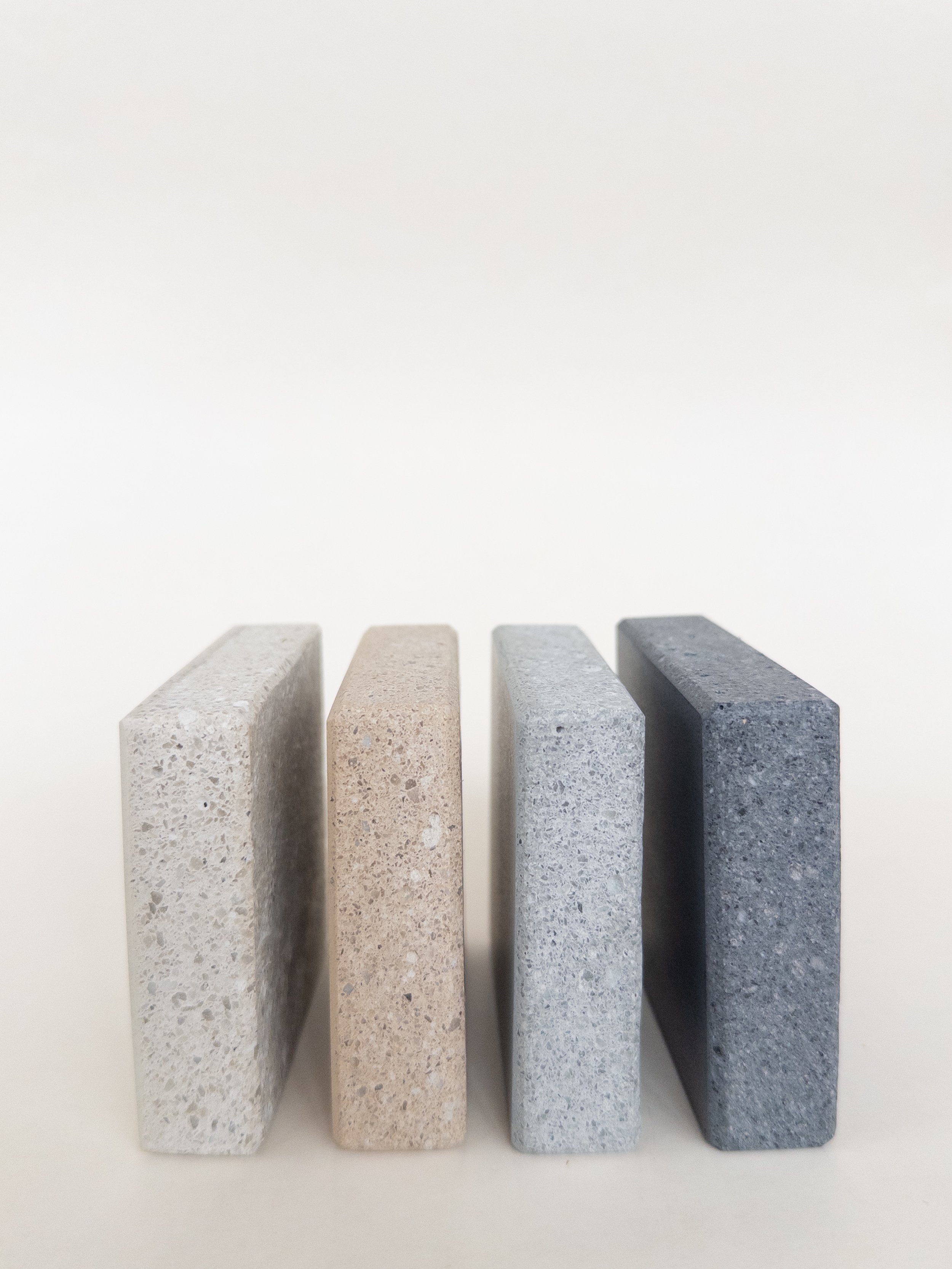 Four rectangular stone samples in varying shades of gray, beige, and blue, standing upright on a white surface against a white background.
