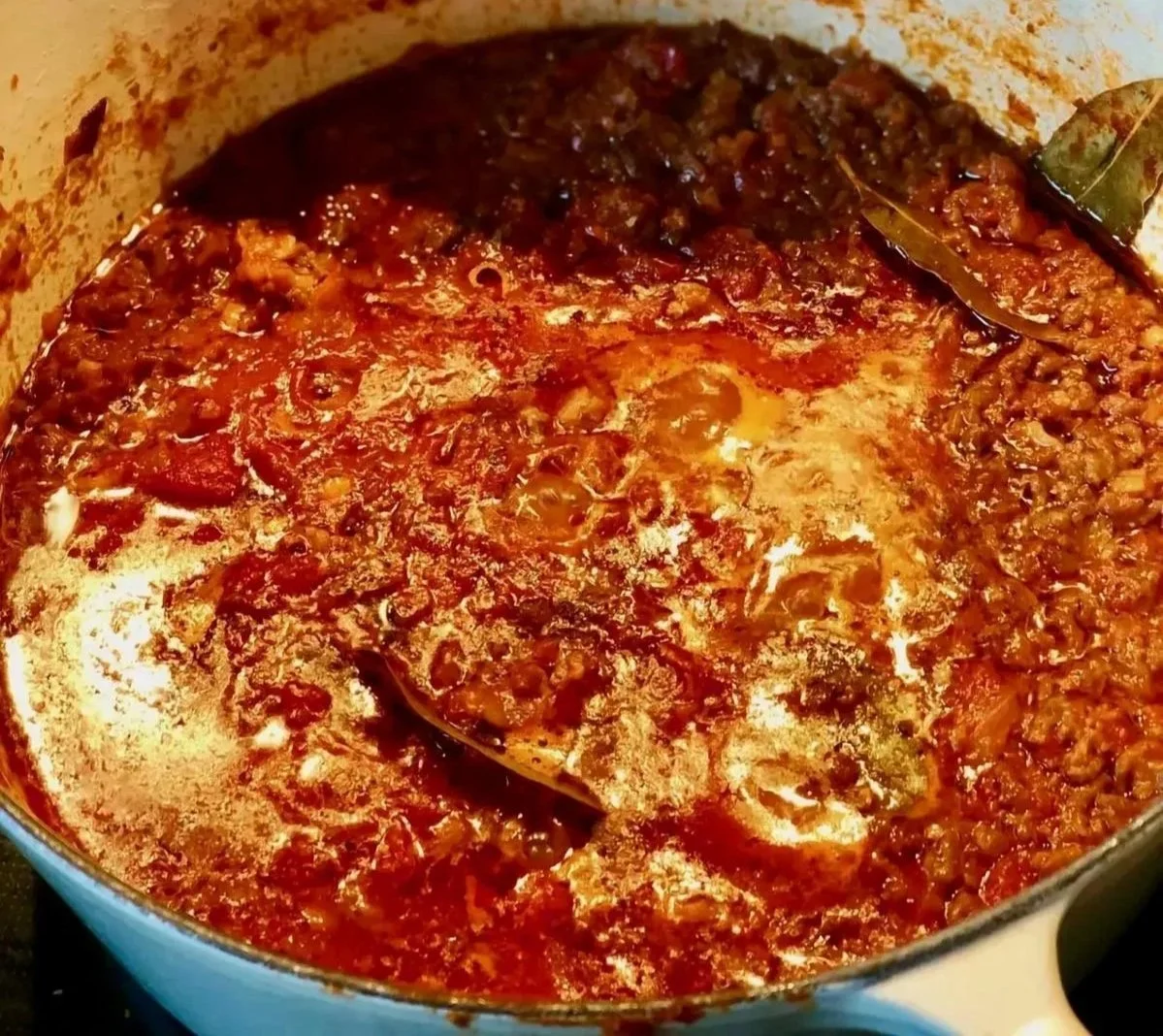 A simmering pot of homemade meat sauce with tomatoes, ground meat, and spices.
