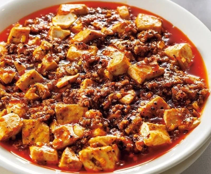A white bowl filled with mapo tofu, featuring tofu cubes and minced meat in a spicy red sauce.
