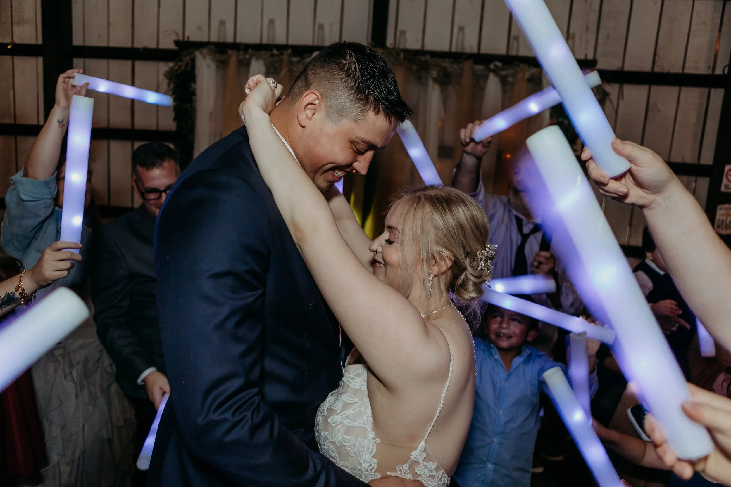 A bride and groom dancing closely at their wedding reception surrounded by guests holding glowing light sticks