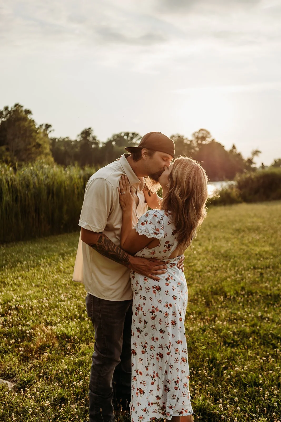 A couple kissing outdoors at sunset, surrounded by greenery and open sky.