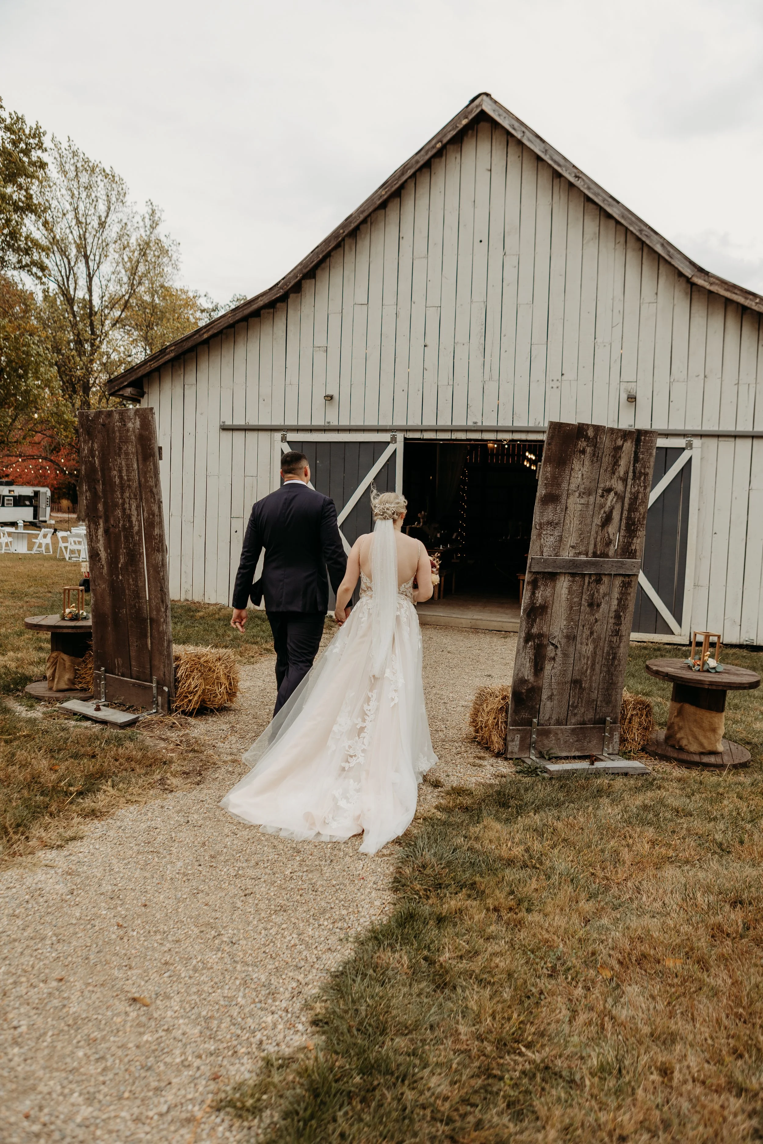 Bride and groom walking towards a barn entrance at a rustic outdoor wedding venue.
