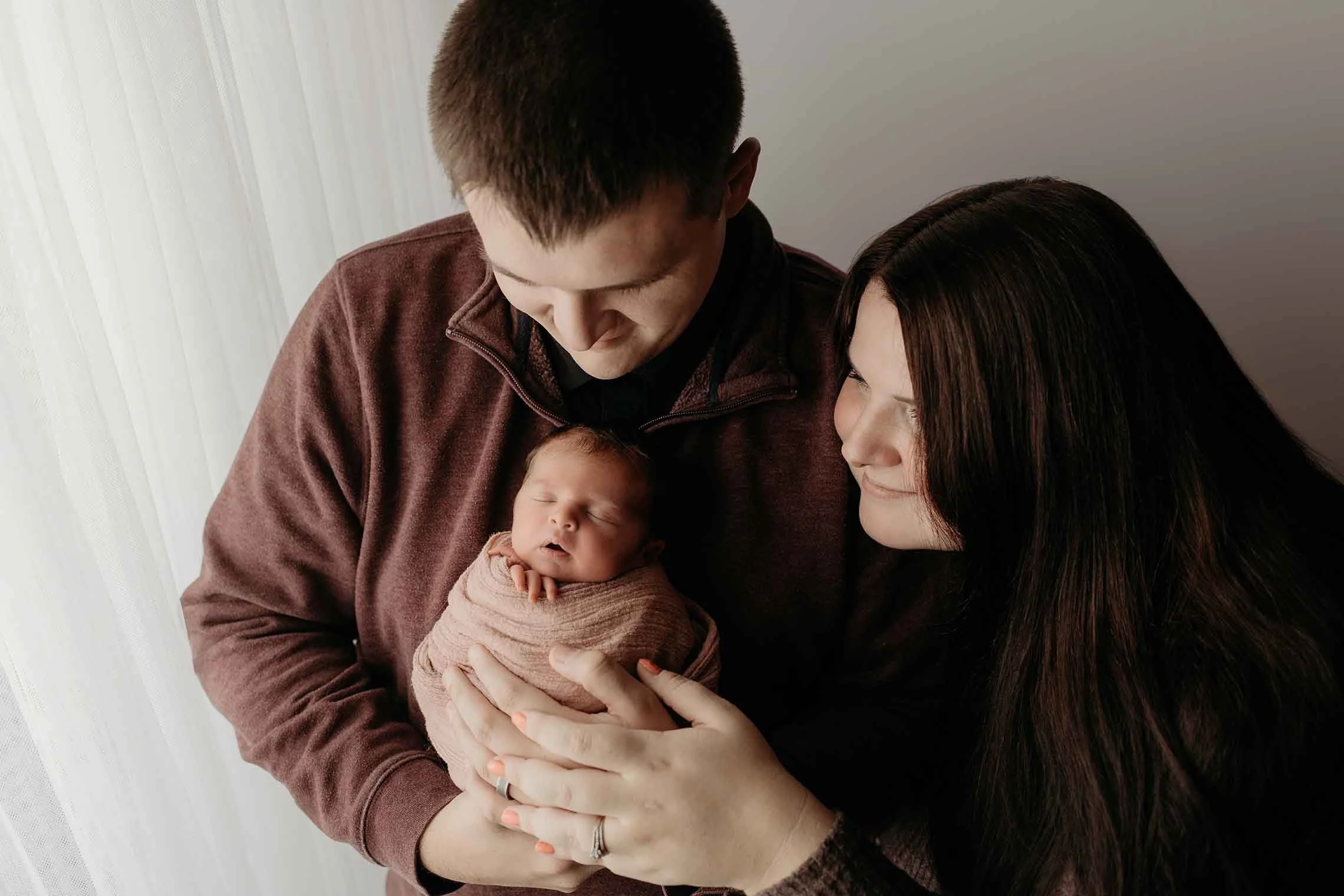 mom & dad holding baby by a window