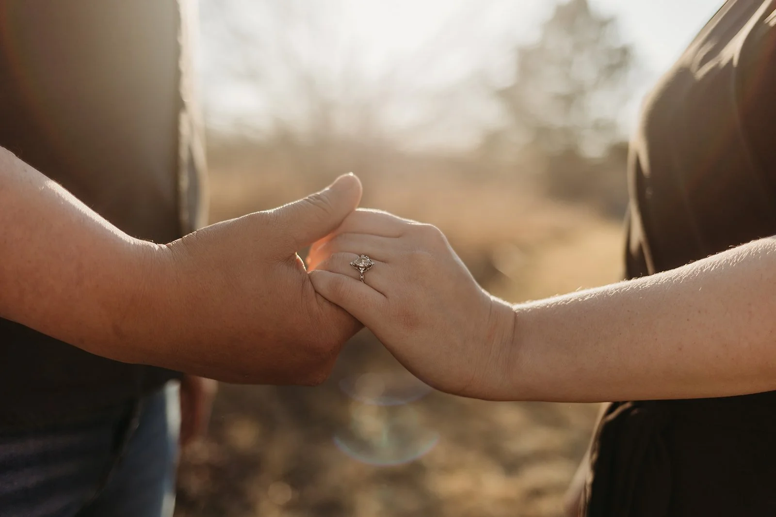 Two people holding hands during sunset, with one person wearing an engagement ring.