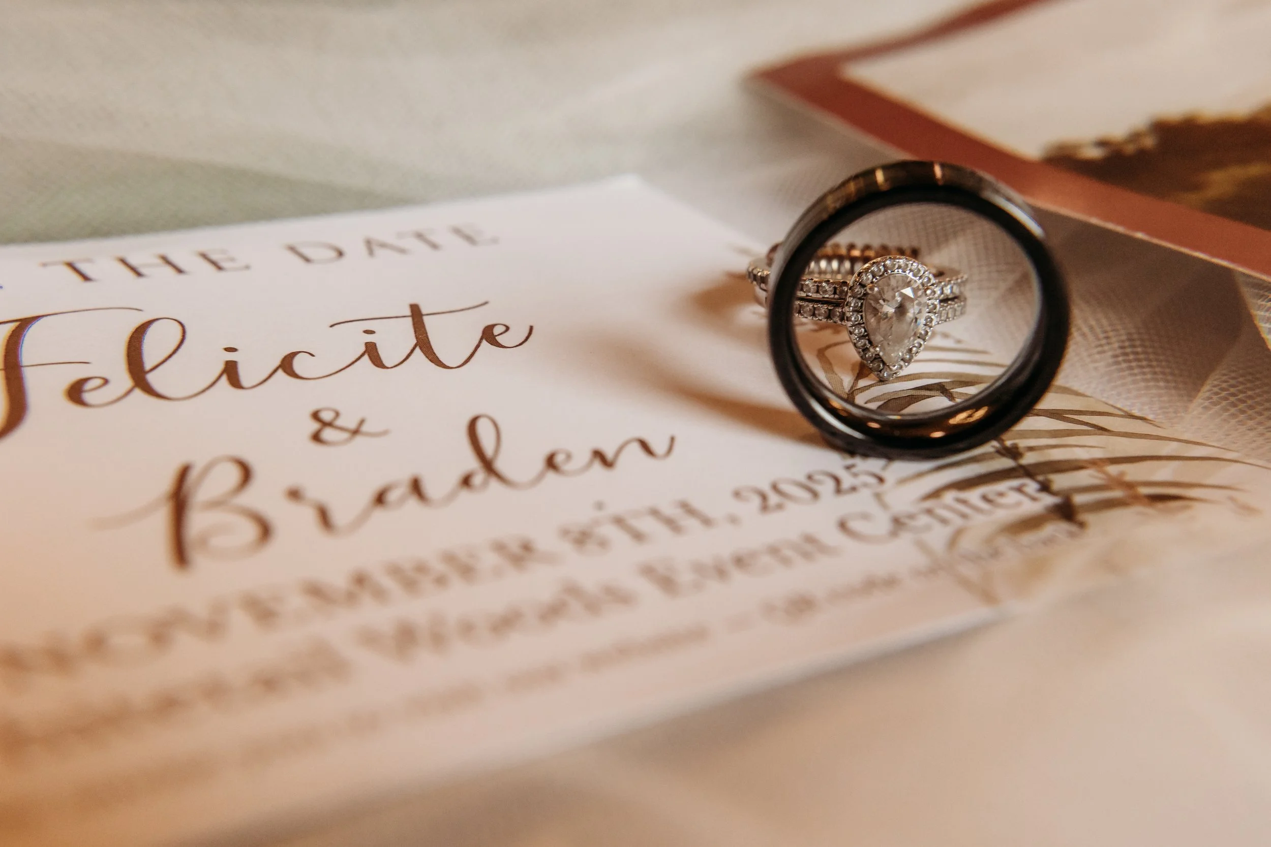 Wedding invitation with a diamond engagement ring and wedding bands placed on top.