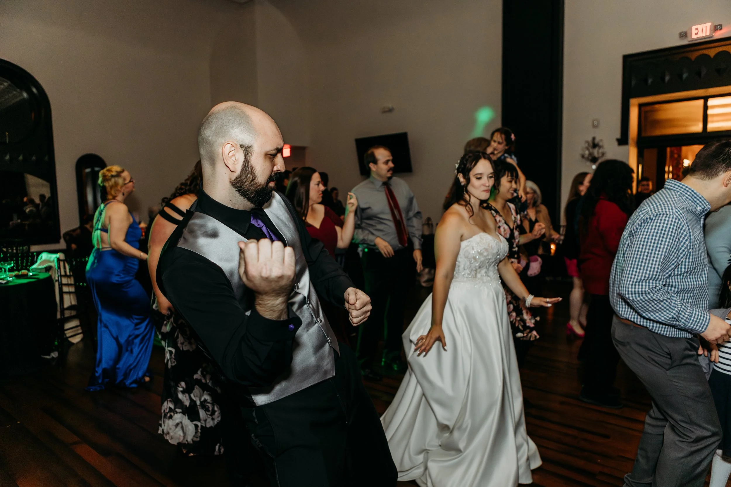People dancing at a wedding reception with a bride in a white gown and a groom in a black shirt with a silver vest.
