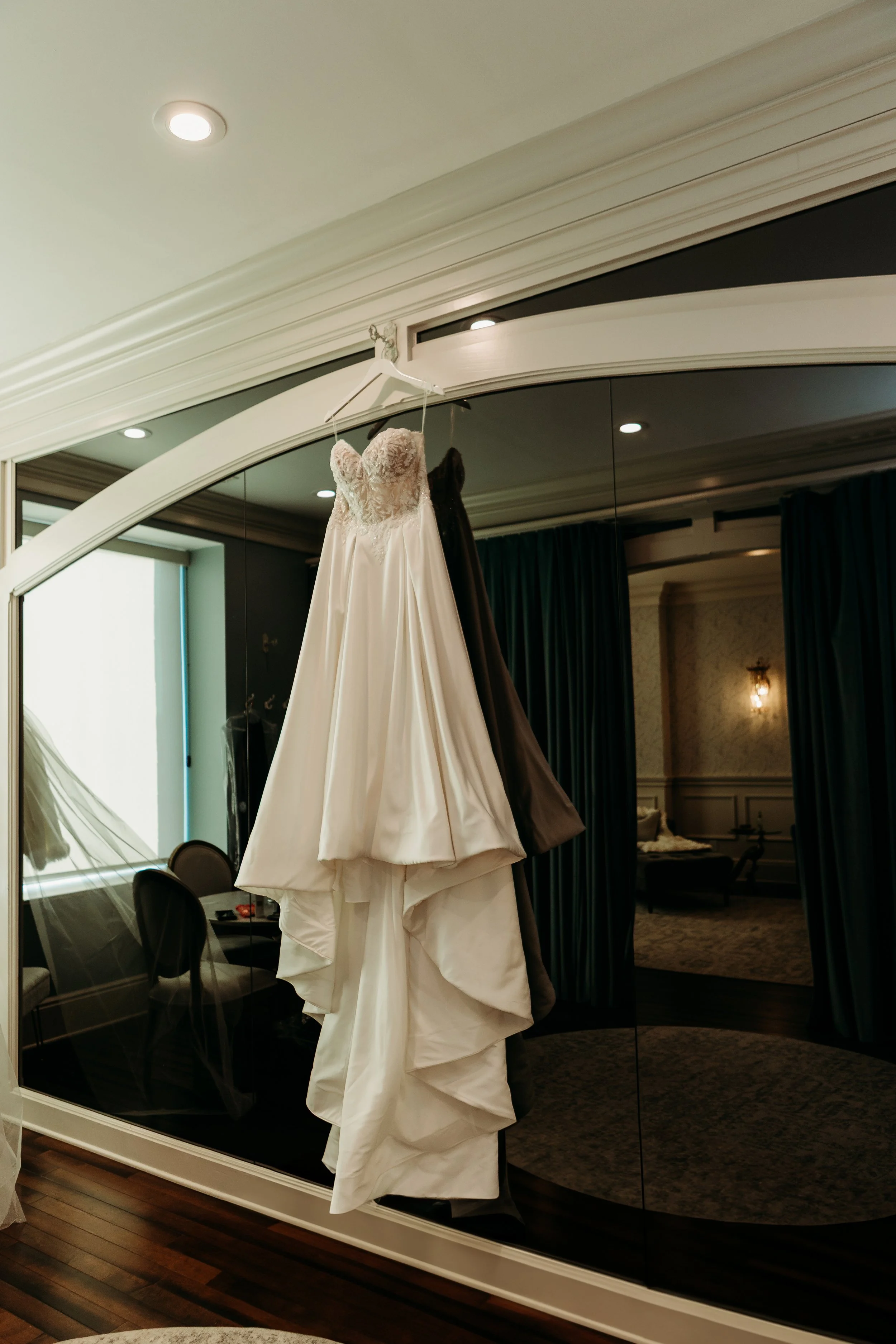 A wedding dress hanging on a hanger in front of a mirror inside a room.