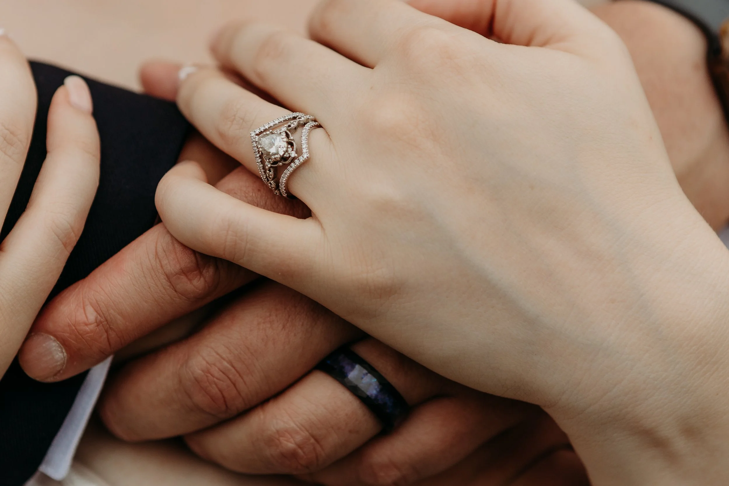 Close-up of two hands with rings, one woman's hand with a silver engagement ring and another person's hand with a black wedding band.