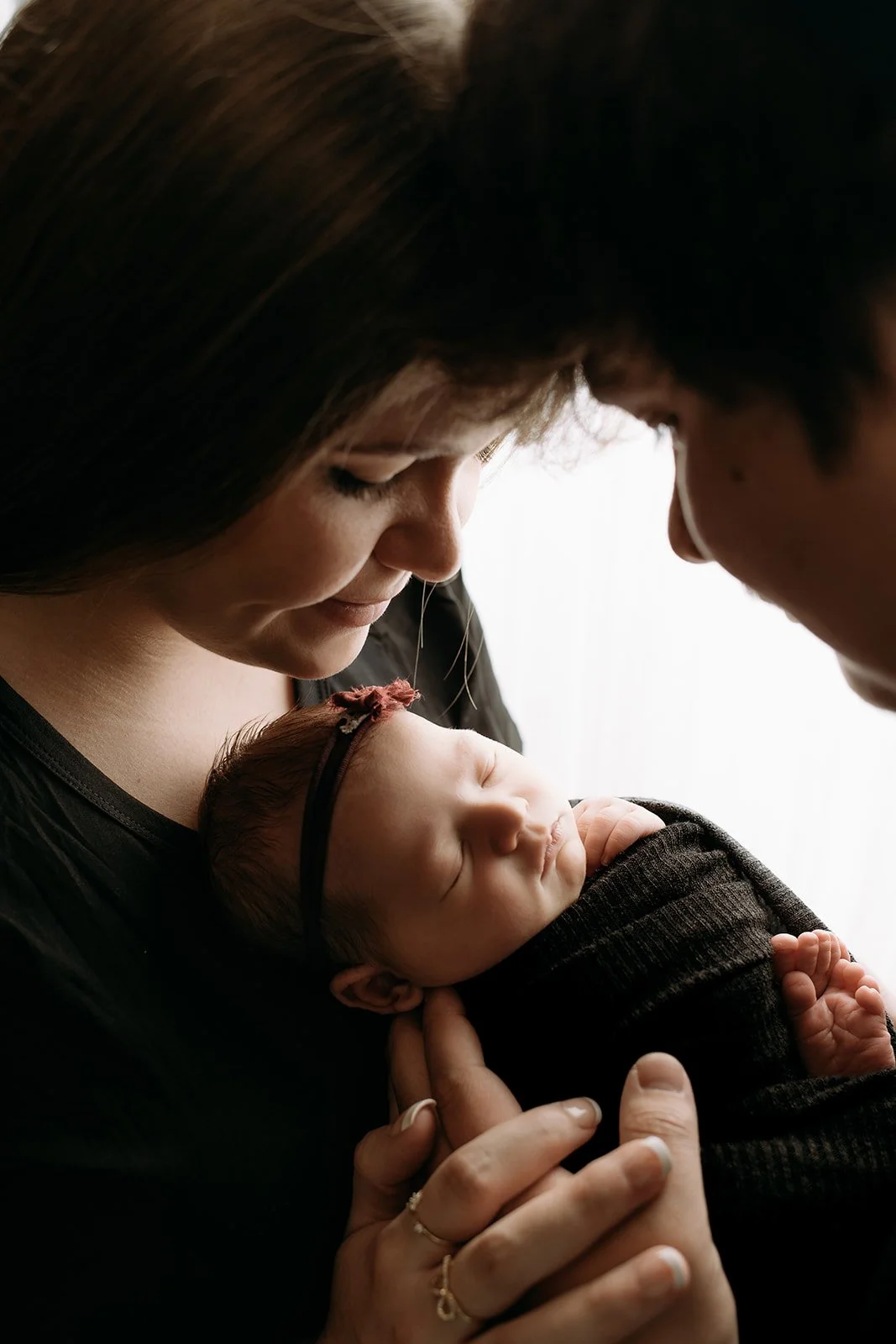 Close-up of a mother holding her sleeping newborn baby, with both faces near each other, showing a tender moment.