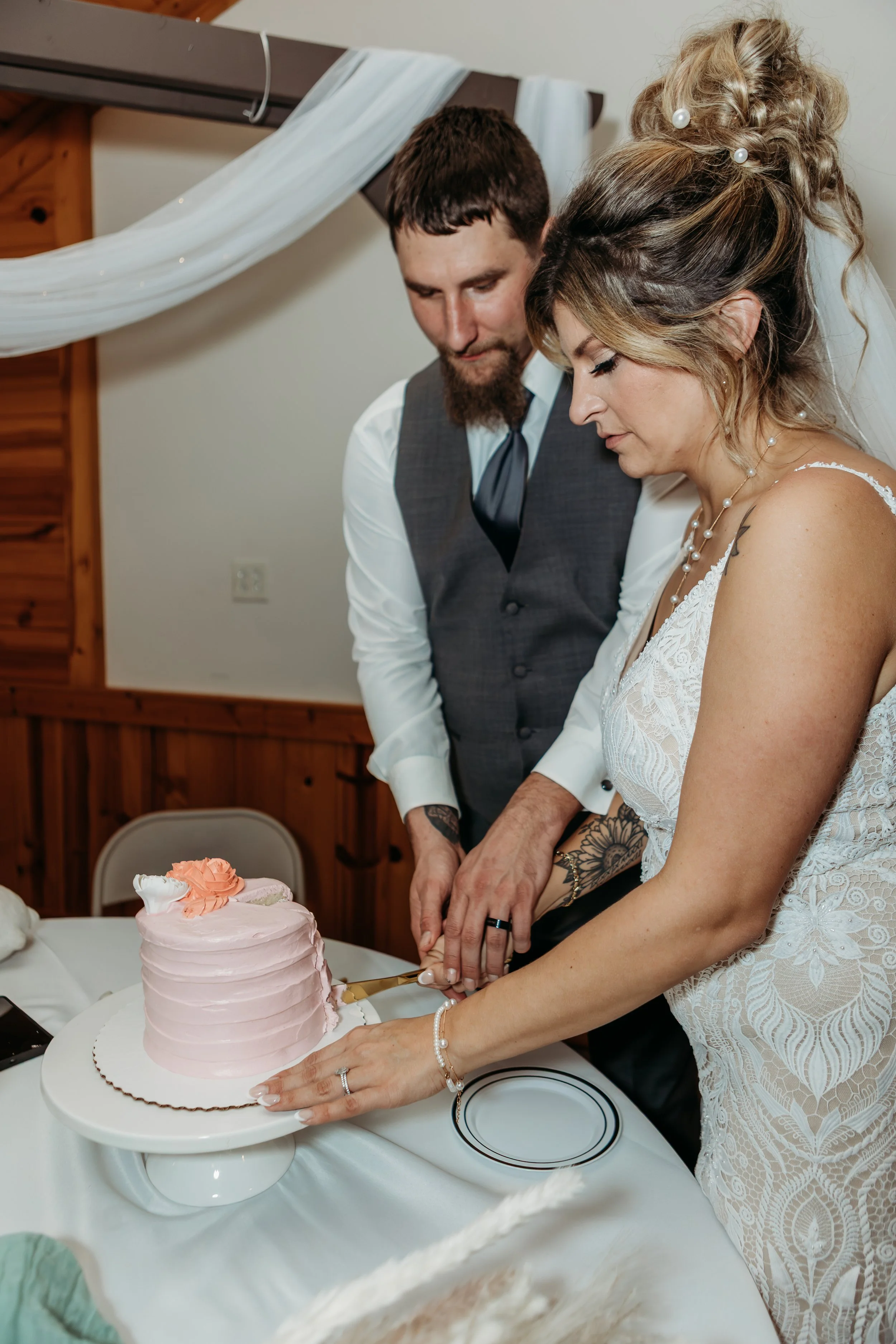 A bride and groom cut a pink wedding cake together at their wedding reception.