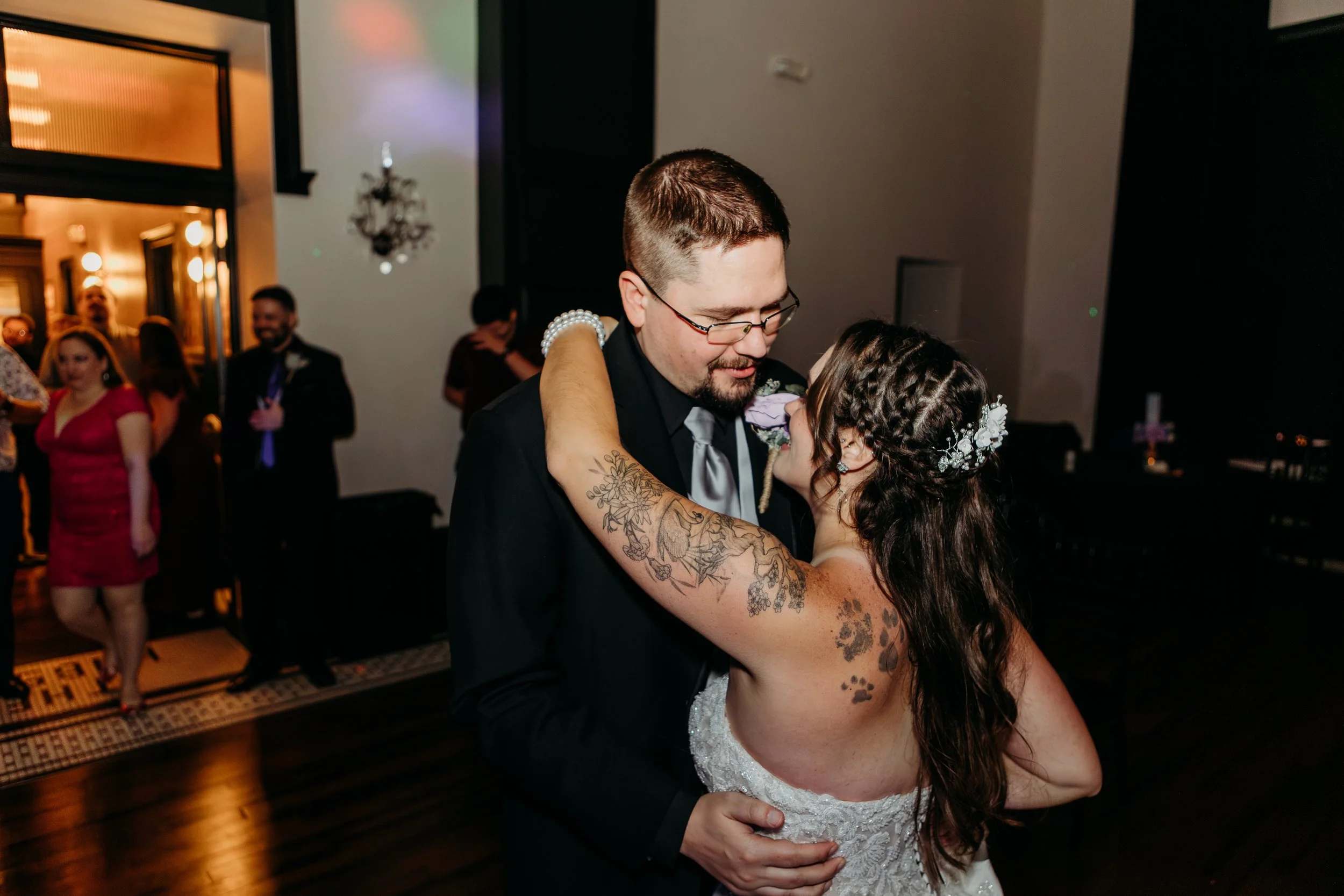 A bride and groom sharing a dance at their wedding reception, with guests in the background.