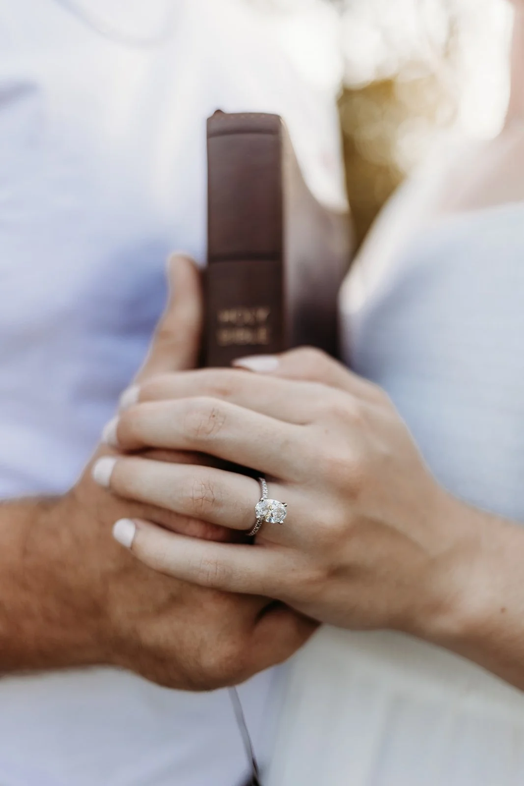 Close-up of a woman wearing an engagement ring with a large diamond, holding a book or box, with a man holding her hand.