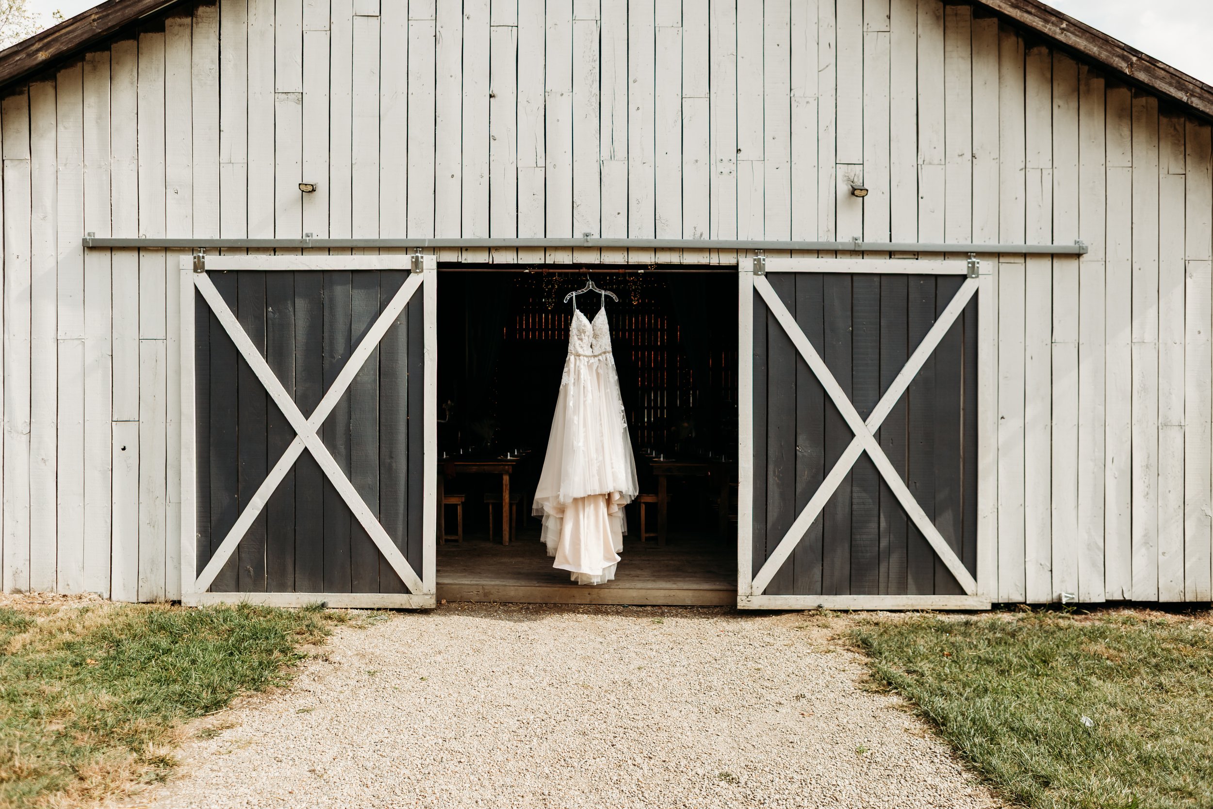 A wedding dress hanging inside a barn on a hanger.